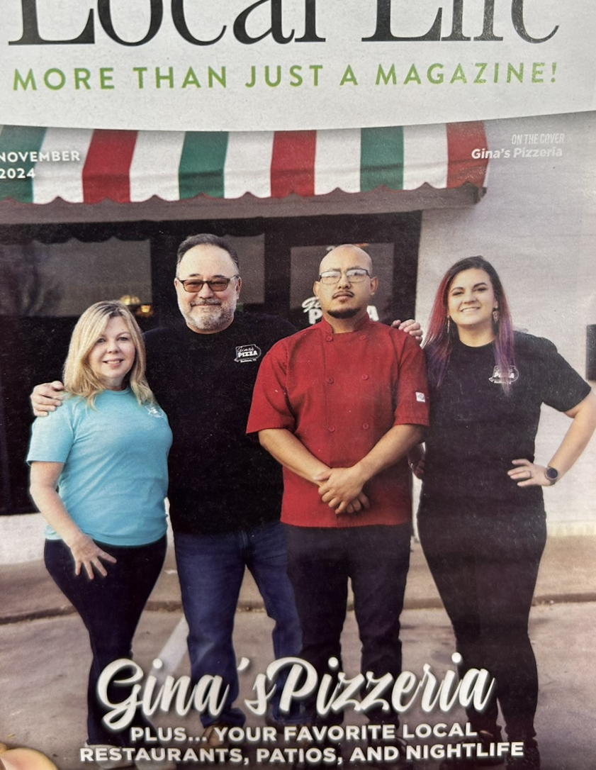Cover of a magazine featuring four people standing in front of a restaurant. The magazine is titled 'Local Life' with the tagline 'More than just a magazine!' The cover mentions Gina's Pizzeria and the date November 2024. The people include two women and two men, one man wearing a red chef's coat, all smiling at the camera.