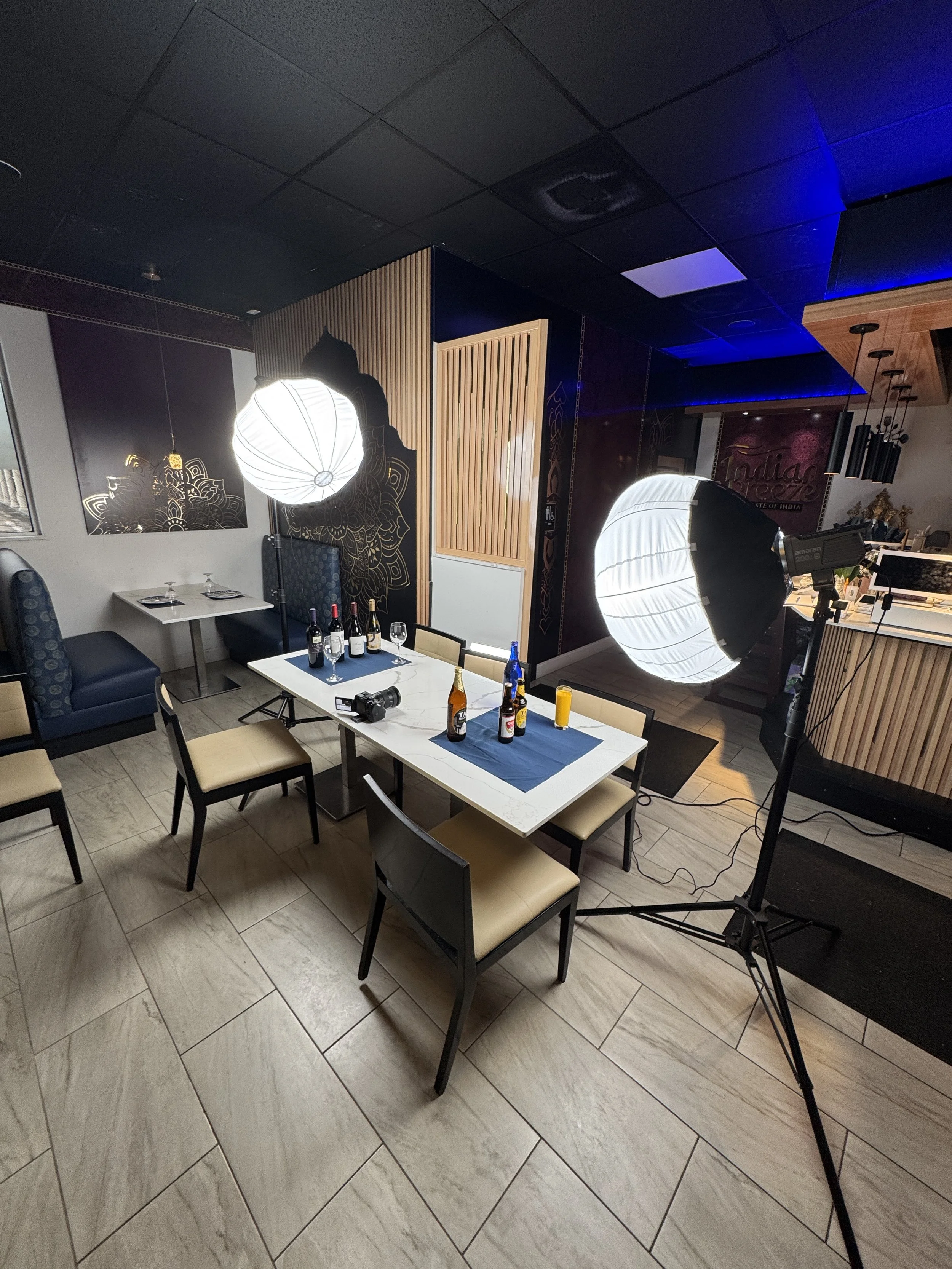 Indoor restaurant or cafe setting with table, chairs, and photography equipment, including large studio lights and a camera on a tripod.