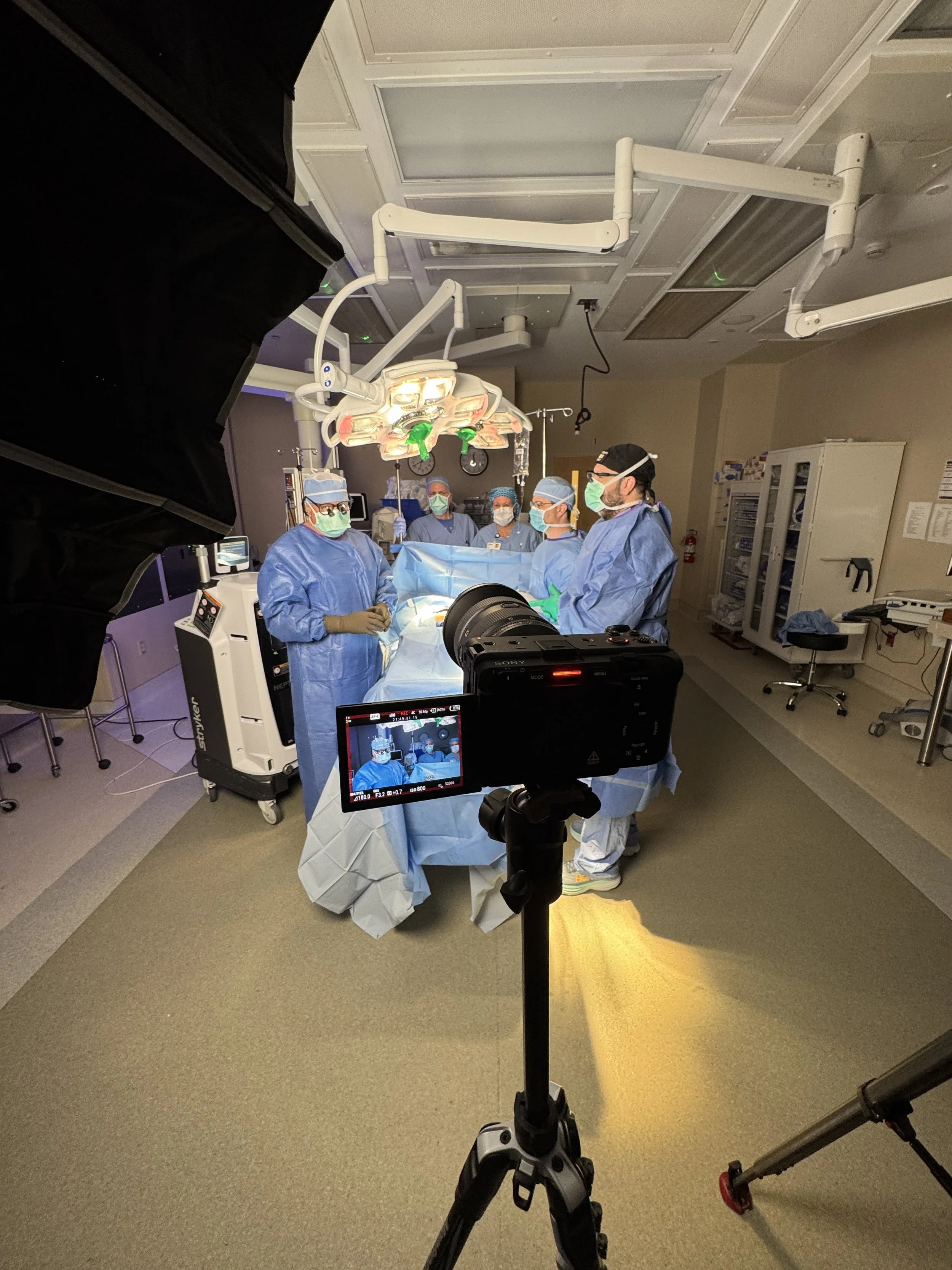 Medical team performing surgery in an operating room, with surgical lights, monitors, and medical equipment.
