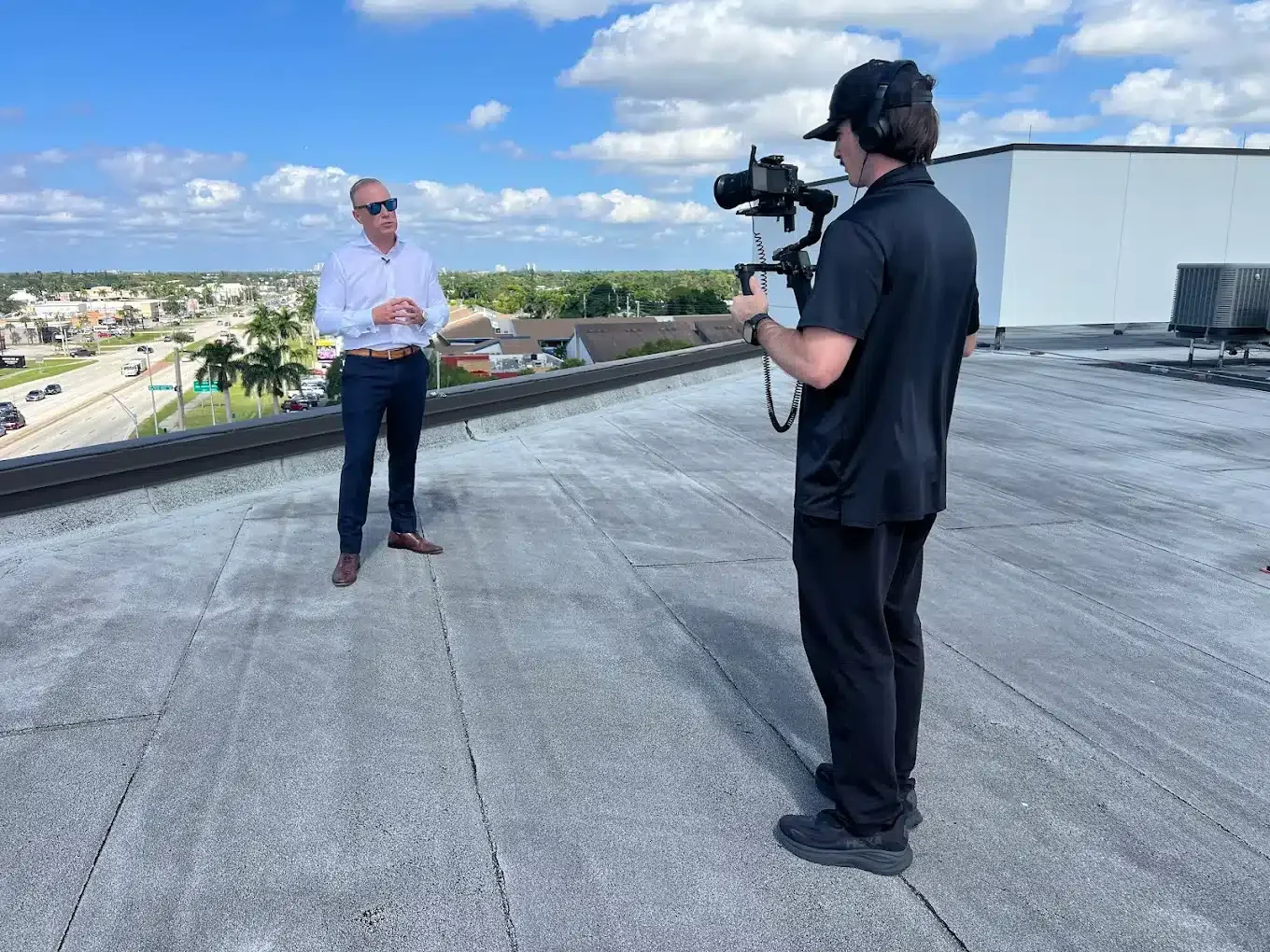 A man in a white shirt and dark pants being filmed on a rooftop by a cameraman with a professional camera.