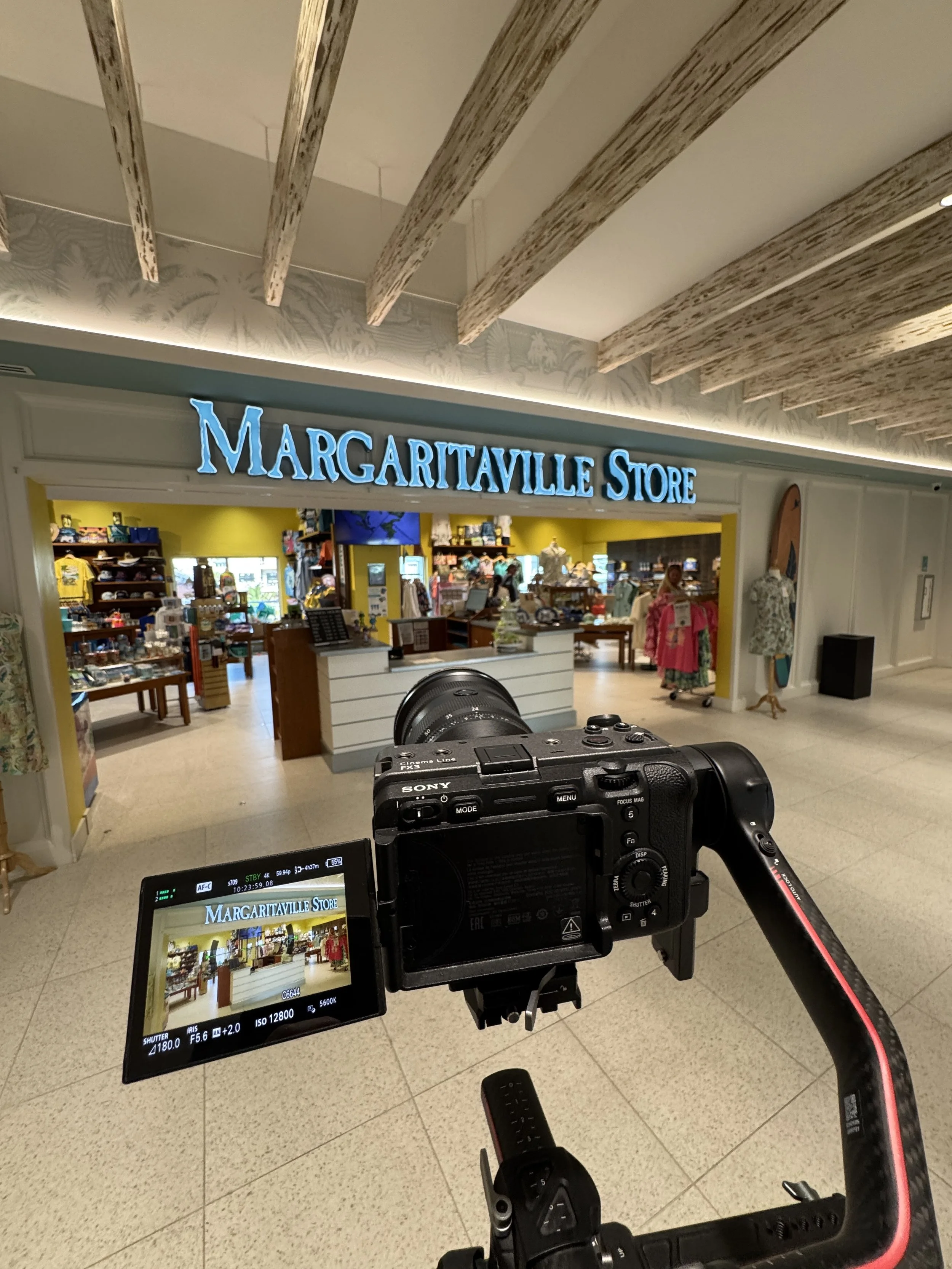 Interior view of the Margaritaville Store with store signage, shelves with merchandise, and mannequins dressed in tropical clothing, while a professional camera is capturing the scene.