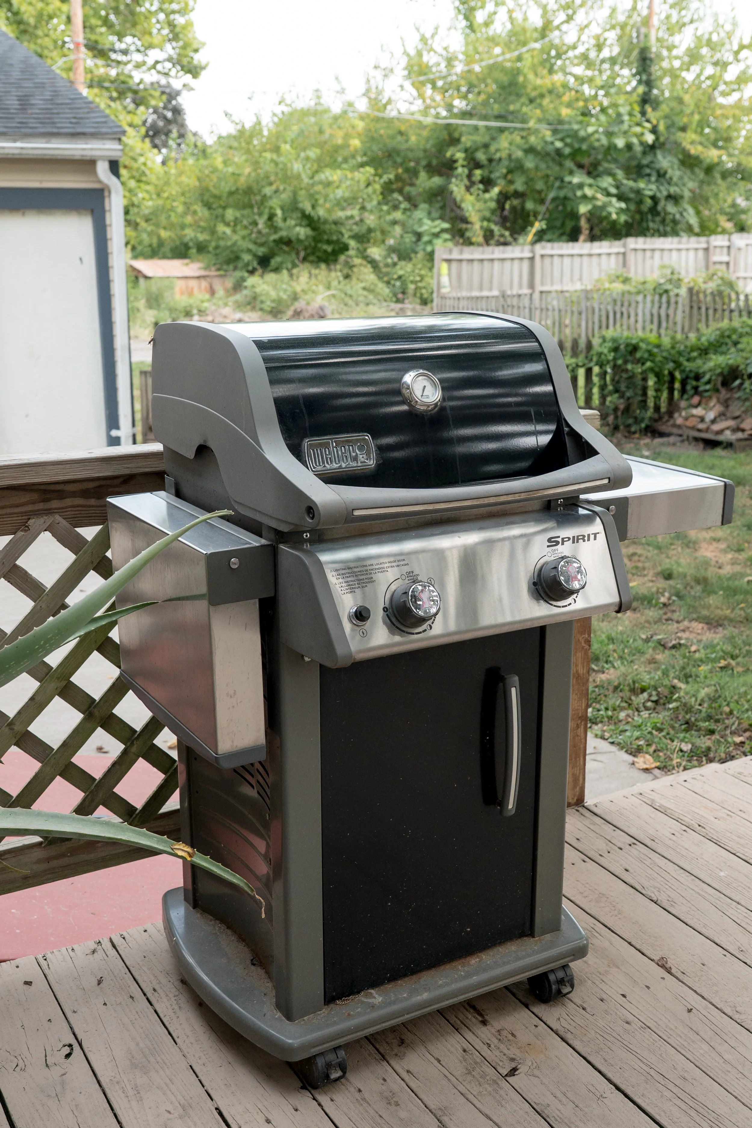 A black and silver Weber Spirit gas grill on a wooden deck outdoors, with a green backyard and trees in the background.