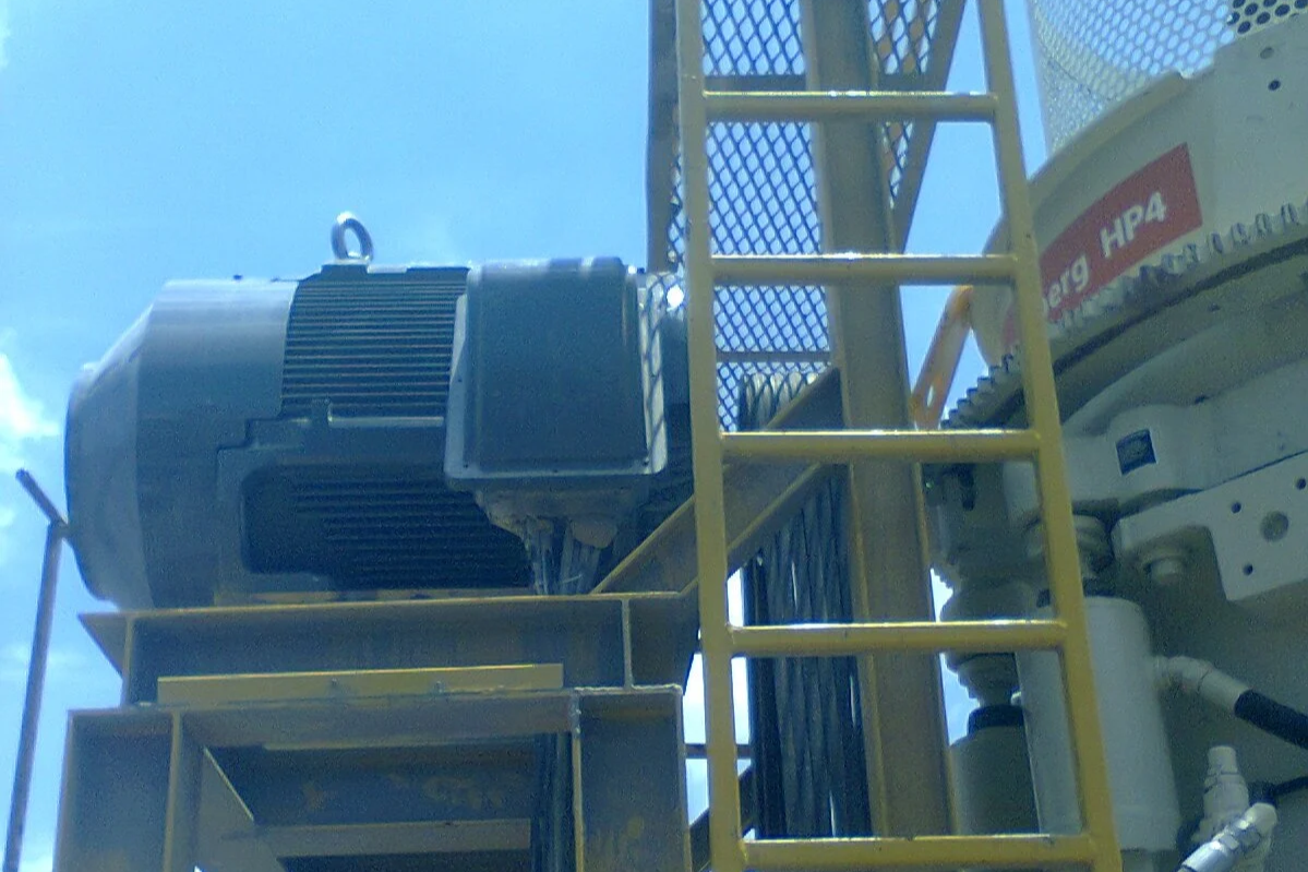 Equipo industrial en una estructura metálica con una escalera amarilla y un motor grande, con el cielo azul de fondo.