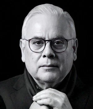 Retrato en blanco y negro de un hombre mayor con gafas, cabello plateado y expresión seria.