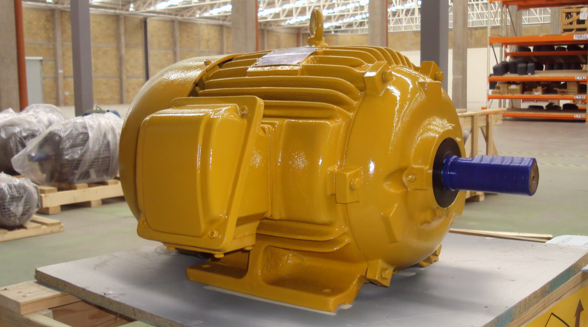 Motor de color amarillo con eje azul, en un almacén industrial.