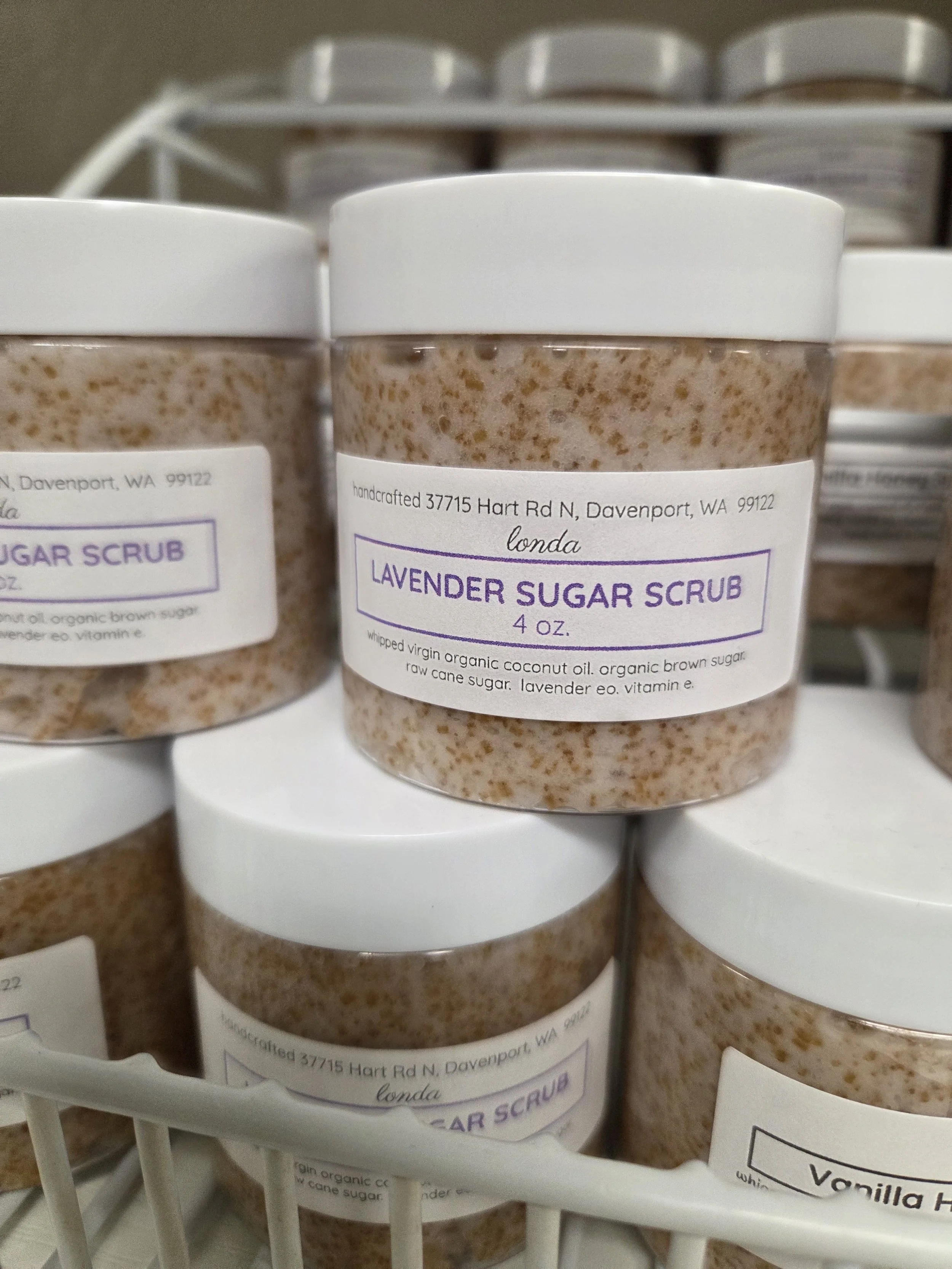 Small jars of lavender sugar scrub with white lids on a store display shelf.
