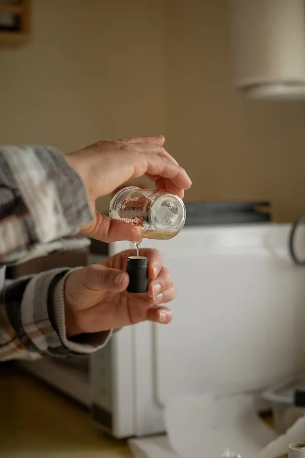 Someone pouring salt from a small glass jar into a salt shaker.