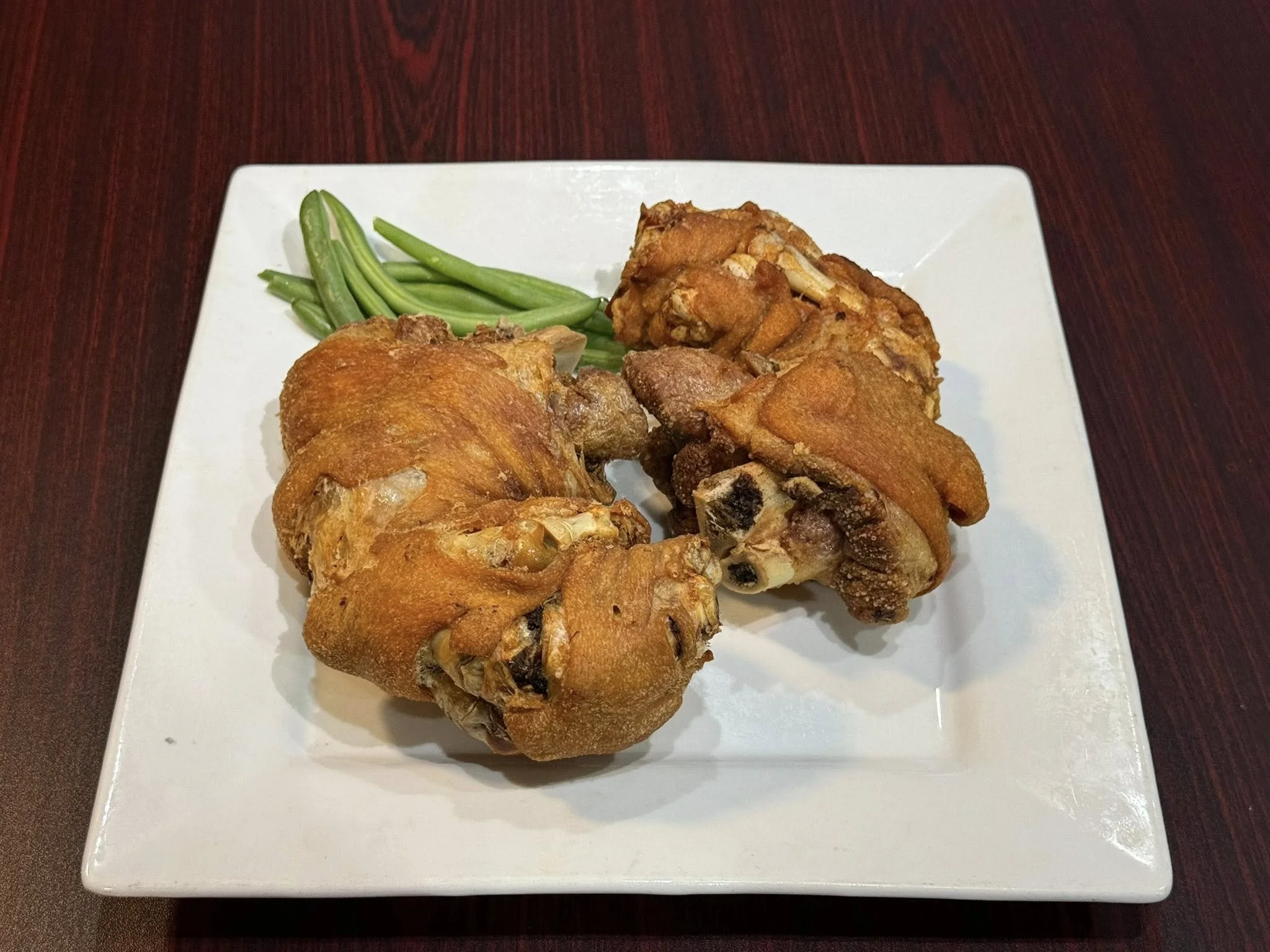 Two pieces of fried chicken with a side of green beans on a white square plate.