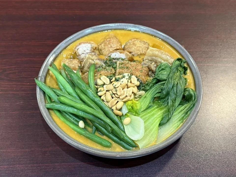 Bowl of curry with green beans, bok choy, peanuts, and tofu on a wooden table