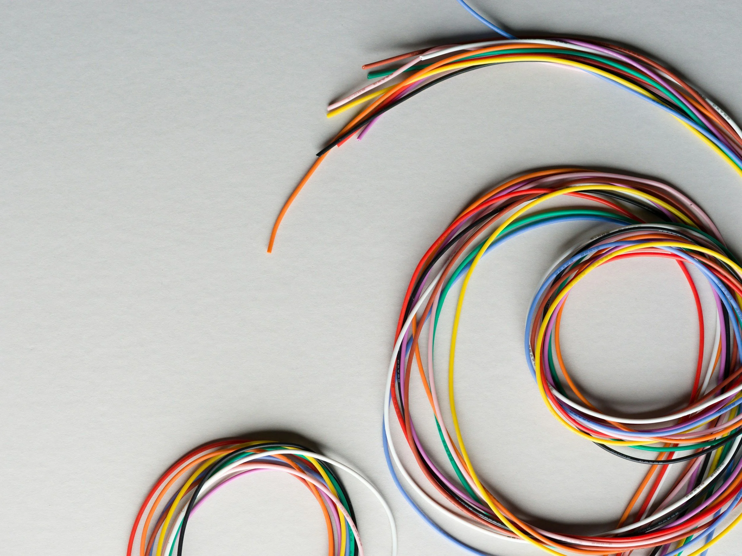 Multiple colorful wires arranged in a spiral on a light grey surface.