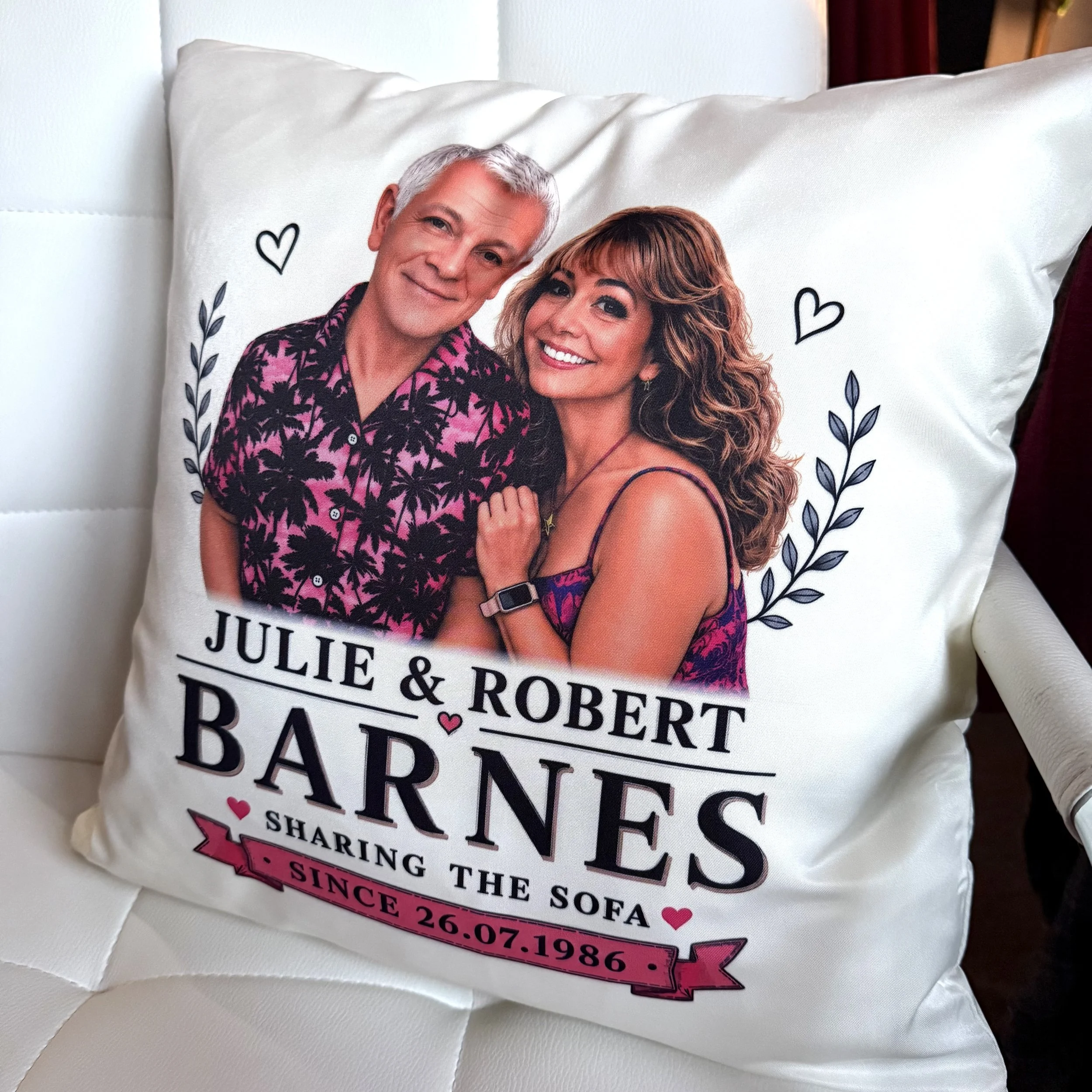 Decorative pillow featuring a photo of a middle-aged man and a woman smiling, surrounded by hearts and floral designs, with partial text showing names and wedding date.
