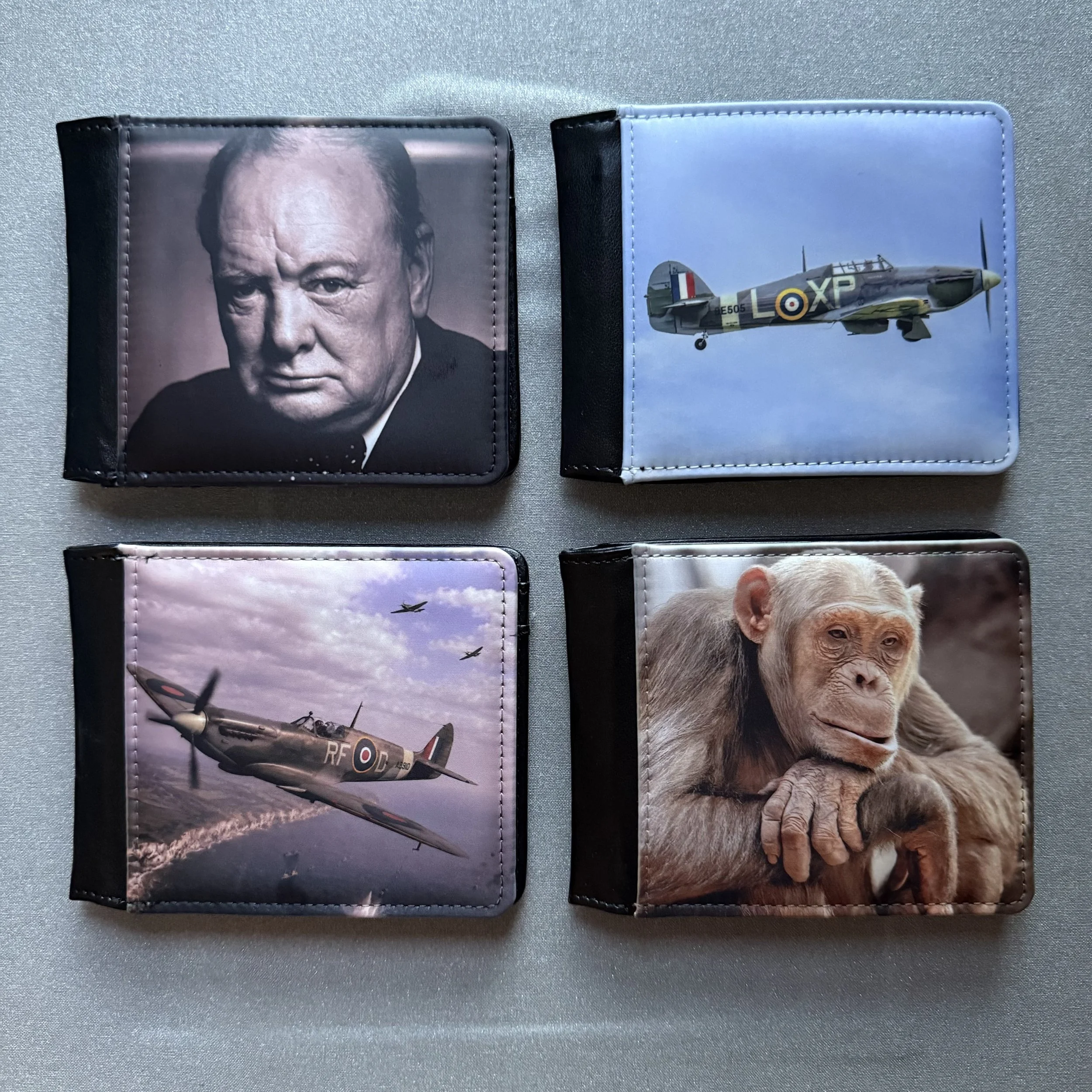 Four photo wallets on a surface. The first wallet features a portrait of a man resembling a political figure. The second wallet shows a fighter jet aircraft in flight. The third wallet depicts an aerial view of fighter jets in formation. The fourth wallet displays a close-up of a chimpanzee's face.