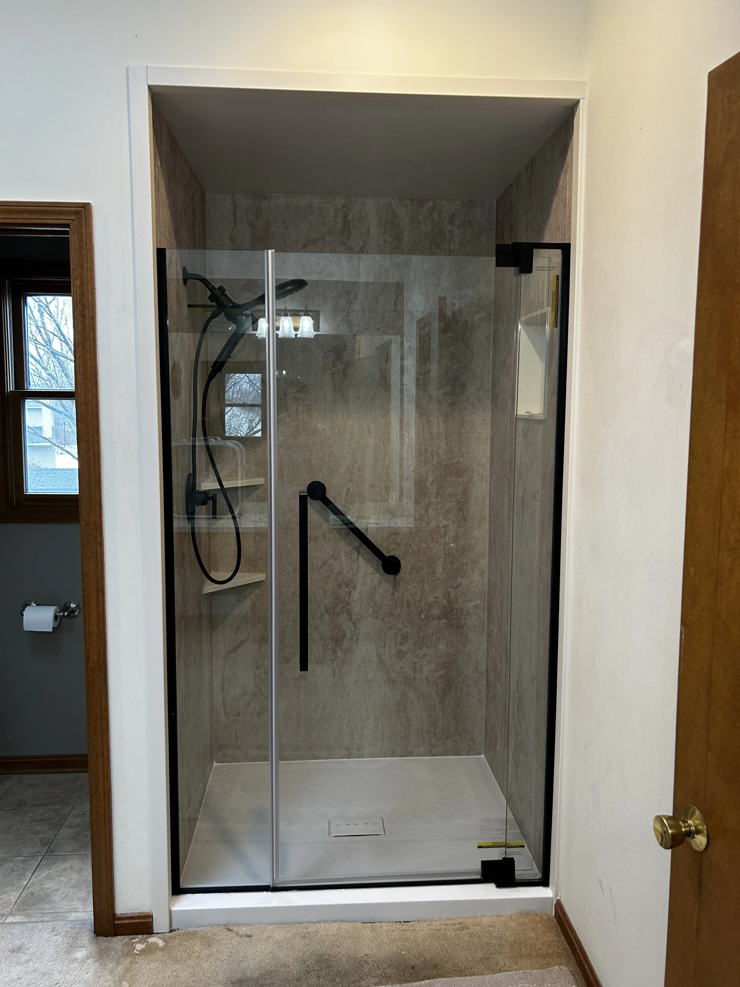 A walk-in shower with glass door and black grab bars.