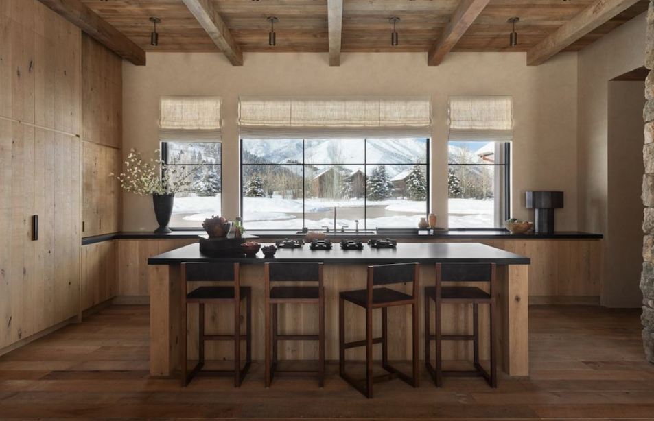 A modern kitchen with wooden cabinets, a large window showing snowy outdoors, and a black countertop island with four wooden chairs.