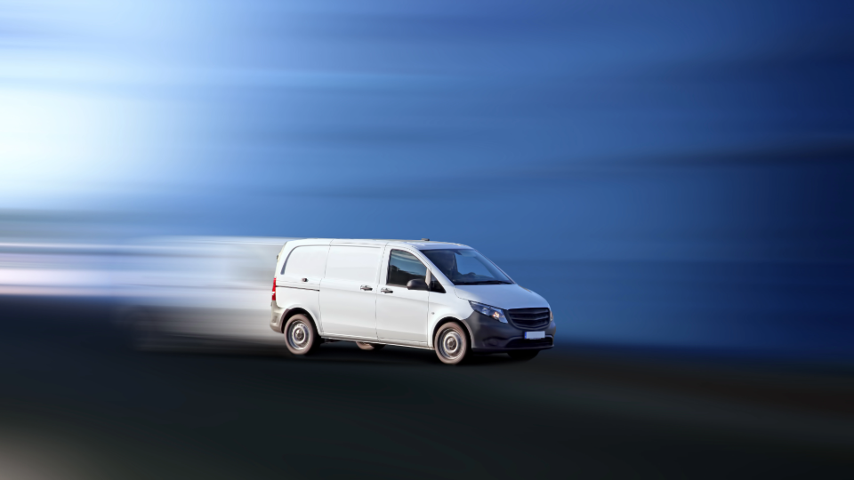 A white cargo van driving on the road with a blurred background and motion blur effect.