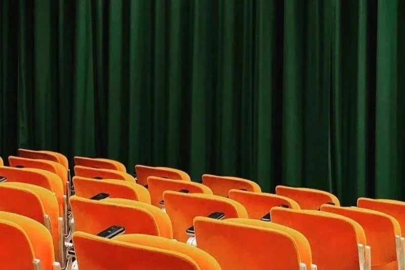 Empty auditorium with orange seats and green curtains.
