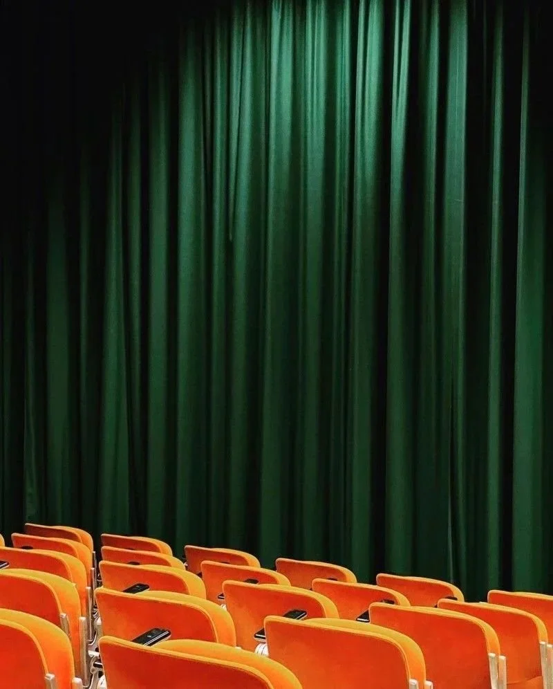 Empty theater with orange seats facing a green curtain.