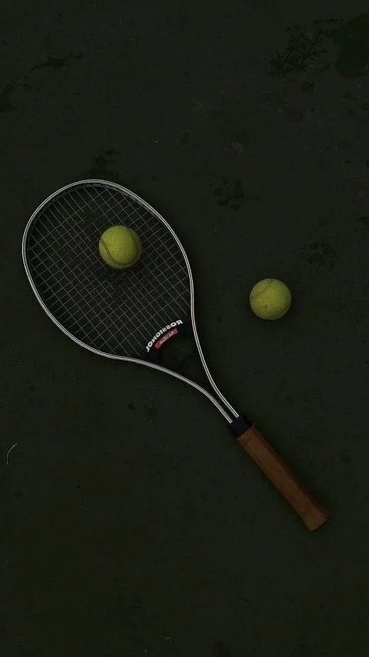 Tennis racket with two tennis balls on a dark court surface.