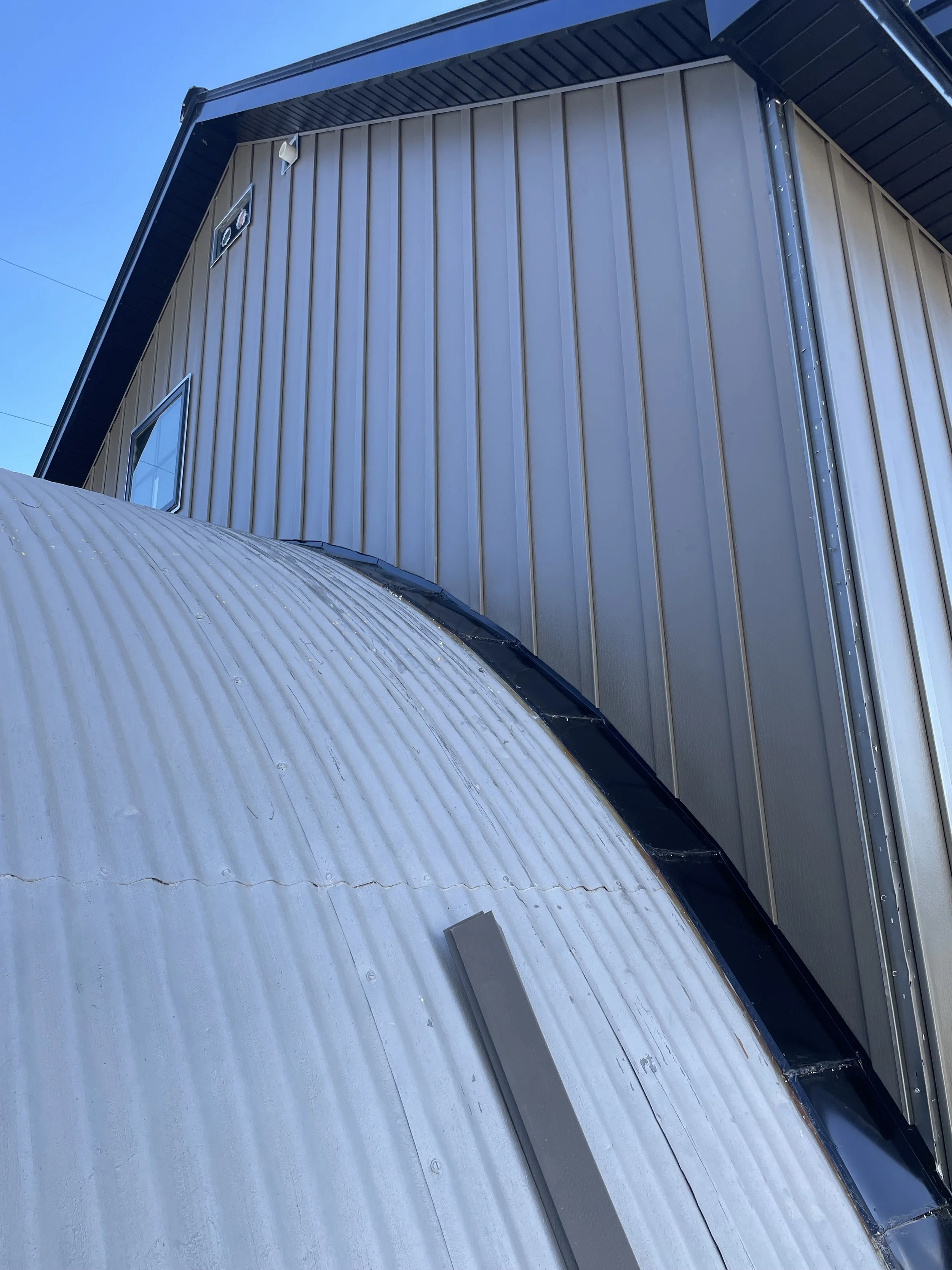 Close-up of a corrugated metal dome and building exterior with a window and vent, under a clear blue sky.