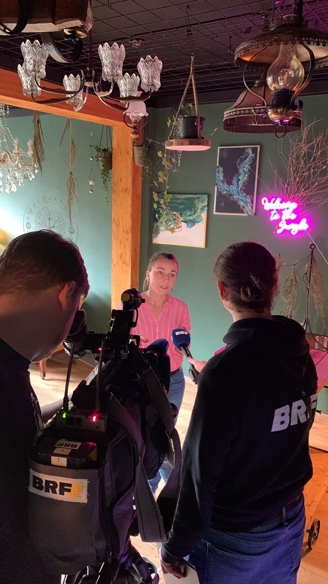Justyna Jakubowska podczas wywiadu medialnego w przytulnym wnętrzu z żyrandolami i roślinami — twórczyni ReflectorLab, specjalistka Human Design prowadząca sesje w języku polskim i niemieckim z Eupen w Belgii