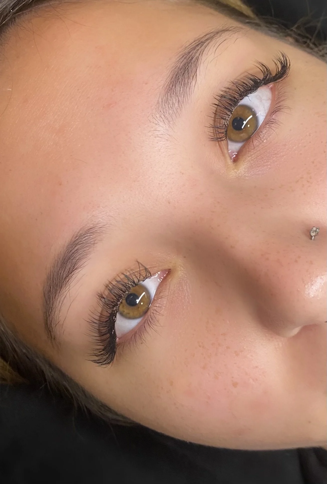 Close-up of a person's face focusing on hazel eyes with long eyelashes, eyebrows, and clear skin.