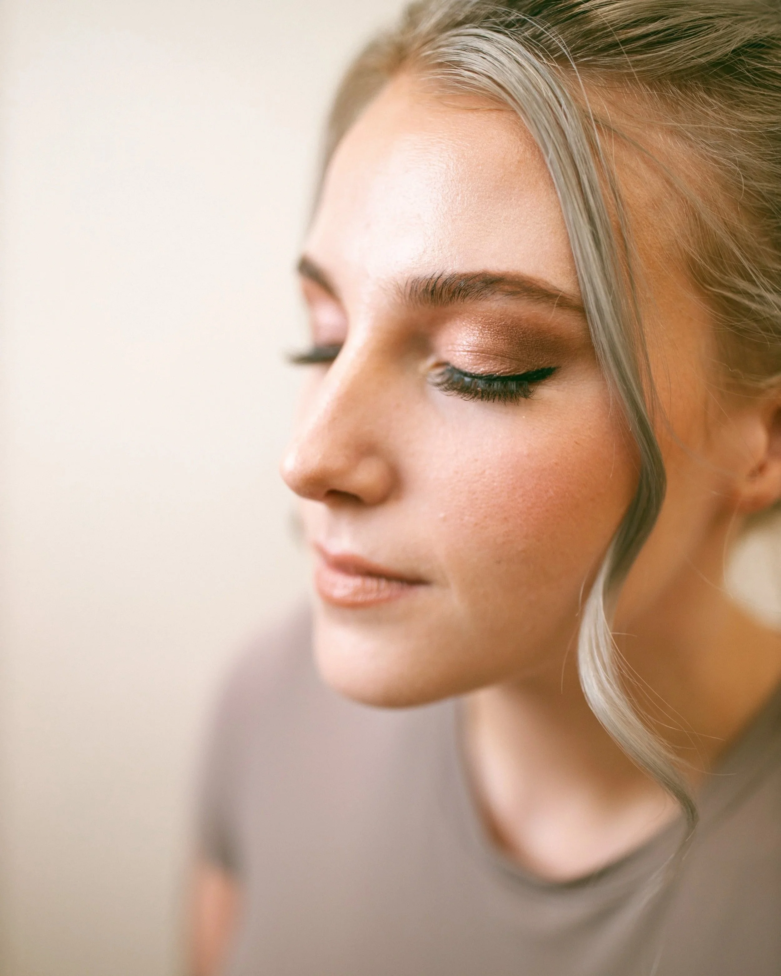 Close-up of a woman's face with eye makeup and blonde hair, with her eyes closed.