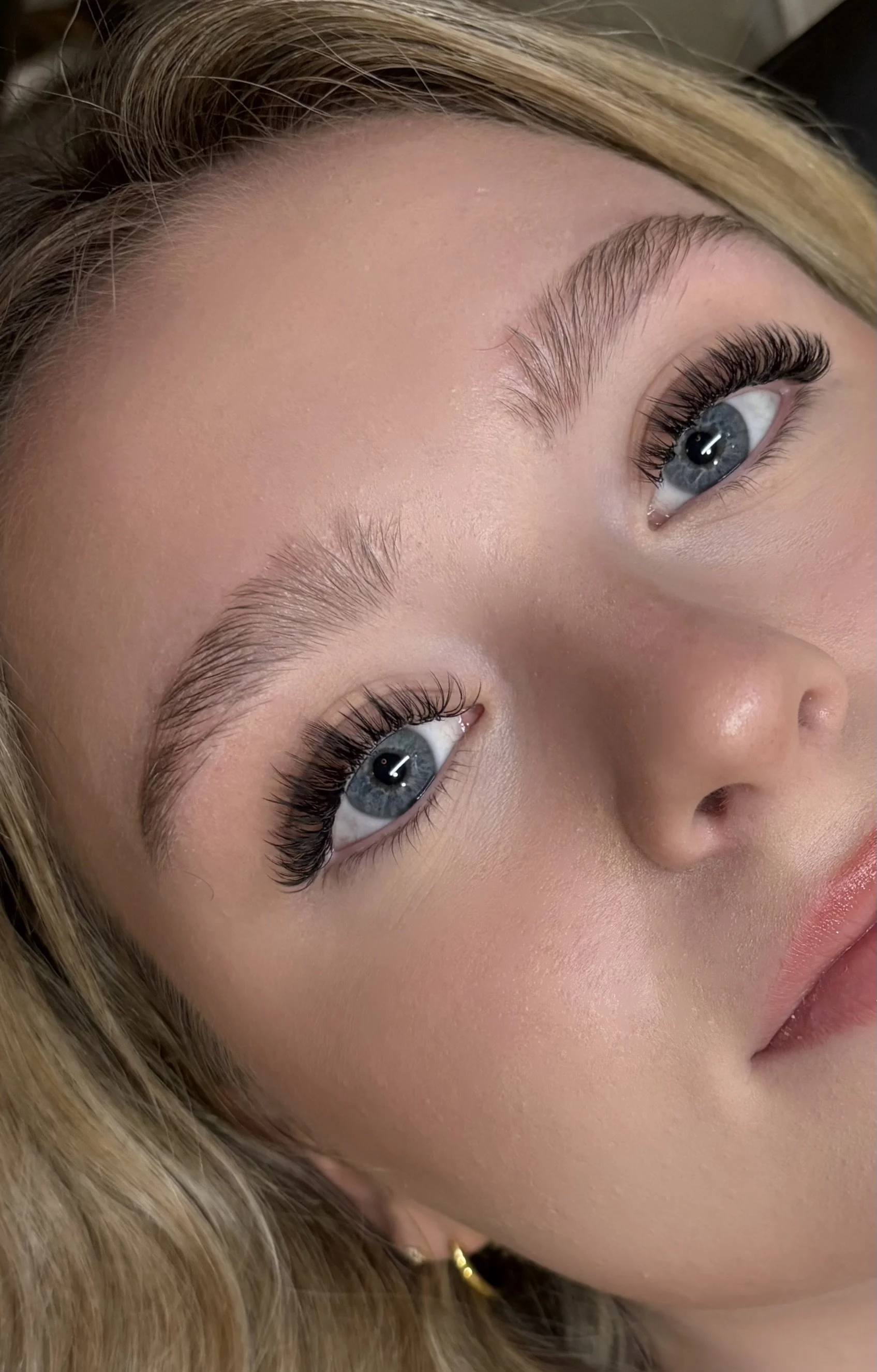 Close-up of a woman's face focusing on her eyes, eyebrows, and part of her cheek. She has long eyelashes, light skin, and blonde hair.
