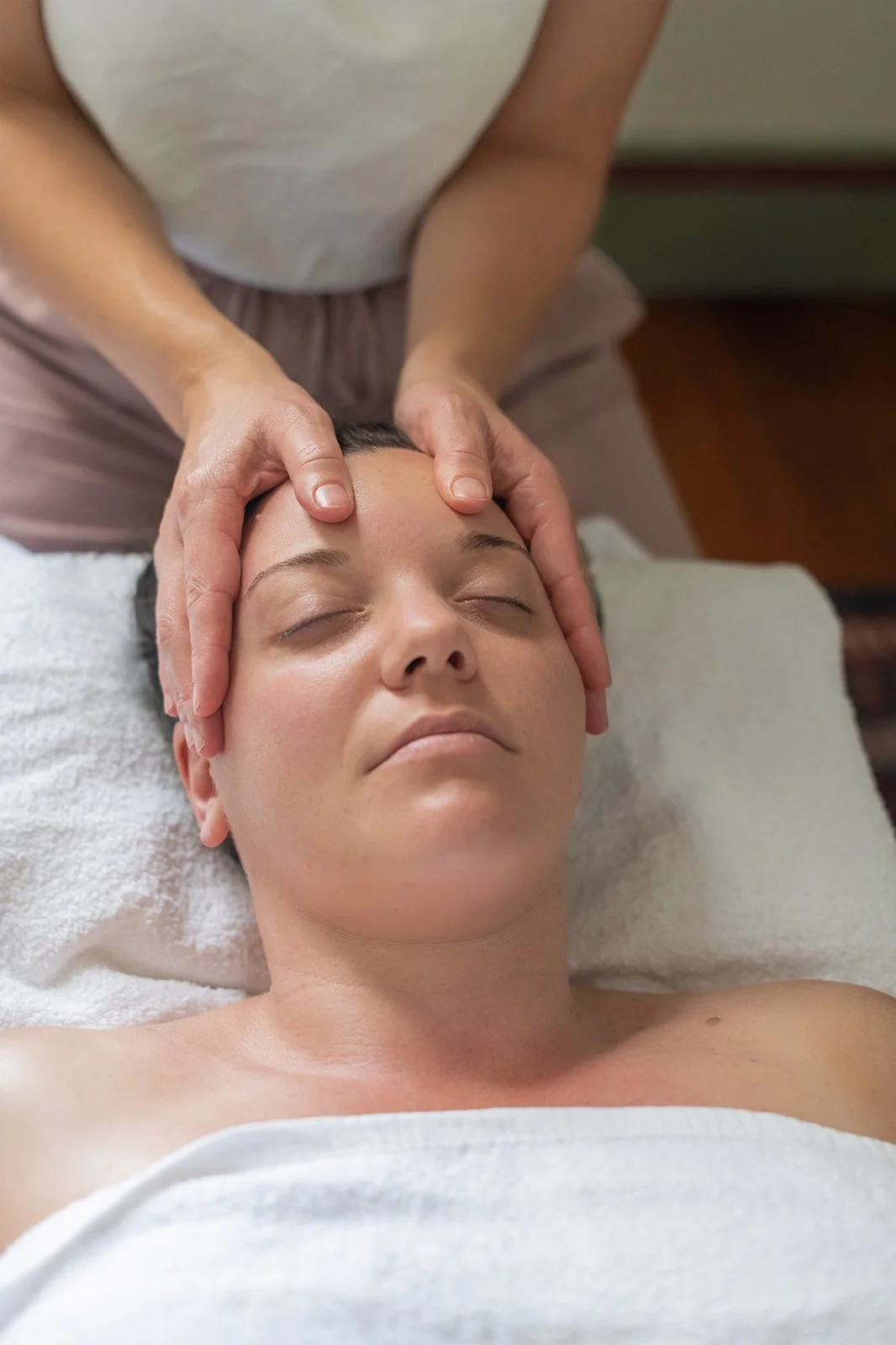 Woman receiving a calming facial massage in Summer Hill. She is lying down with eyes closed, on a treatment table covered with a white towel.