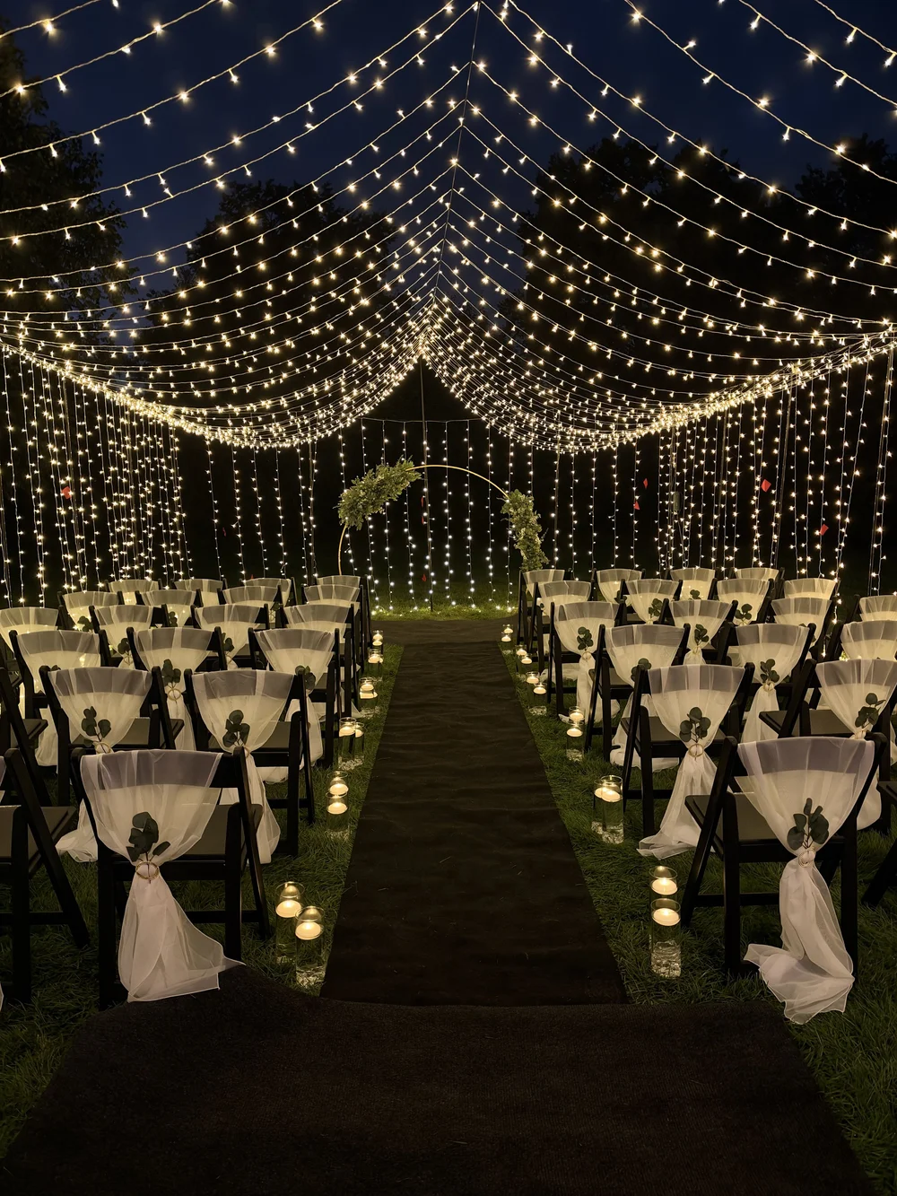 Outdoor vow renewal ceremony beneath a glowing canopy of lights and a floral arch