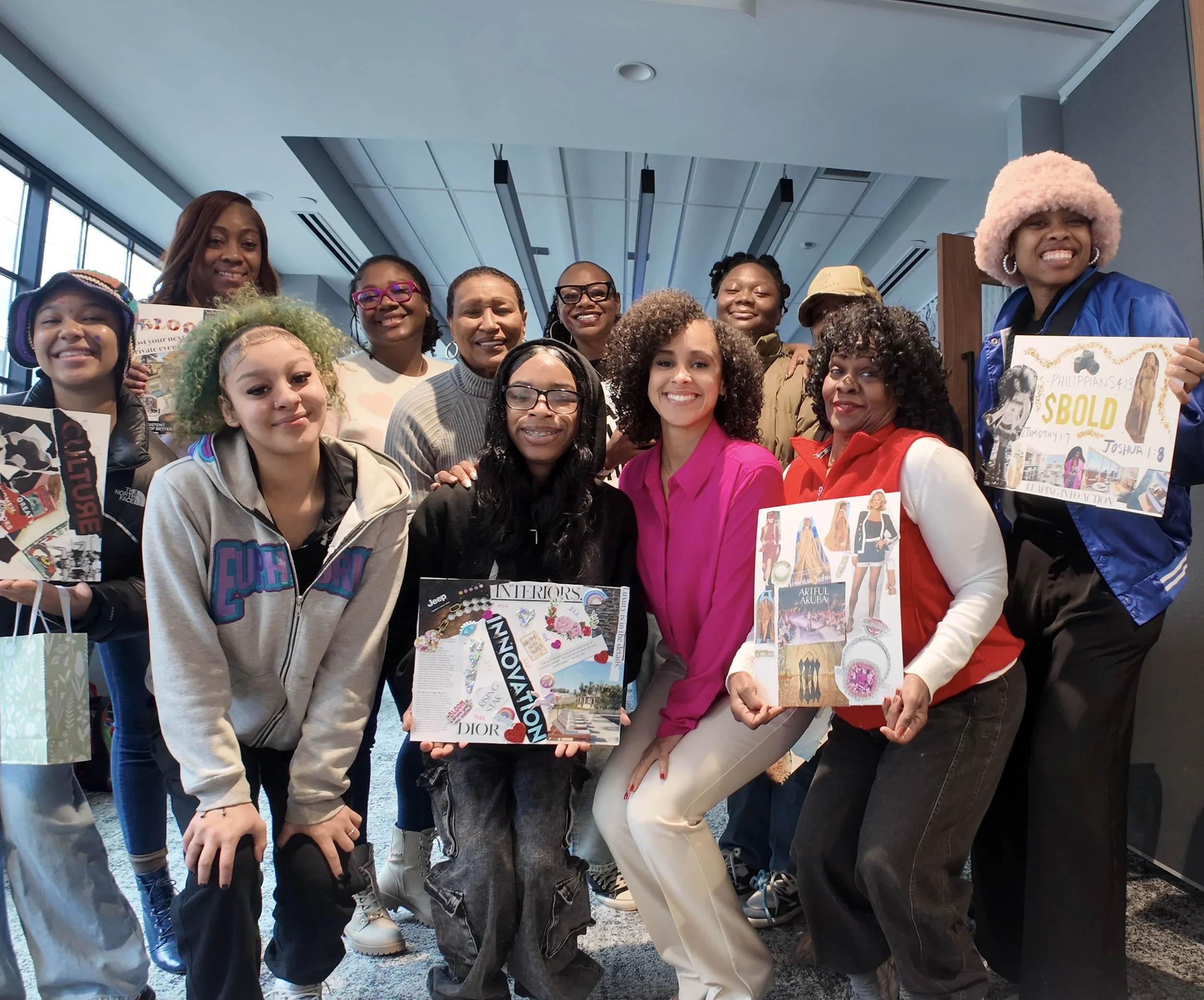 Group of diverse women smiling and holding colorful posters and magazines at an indoor event.