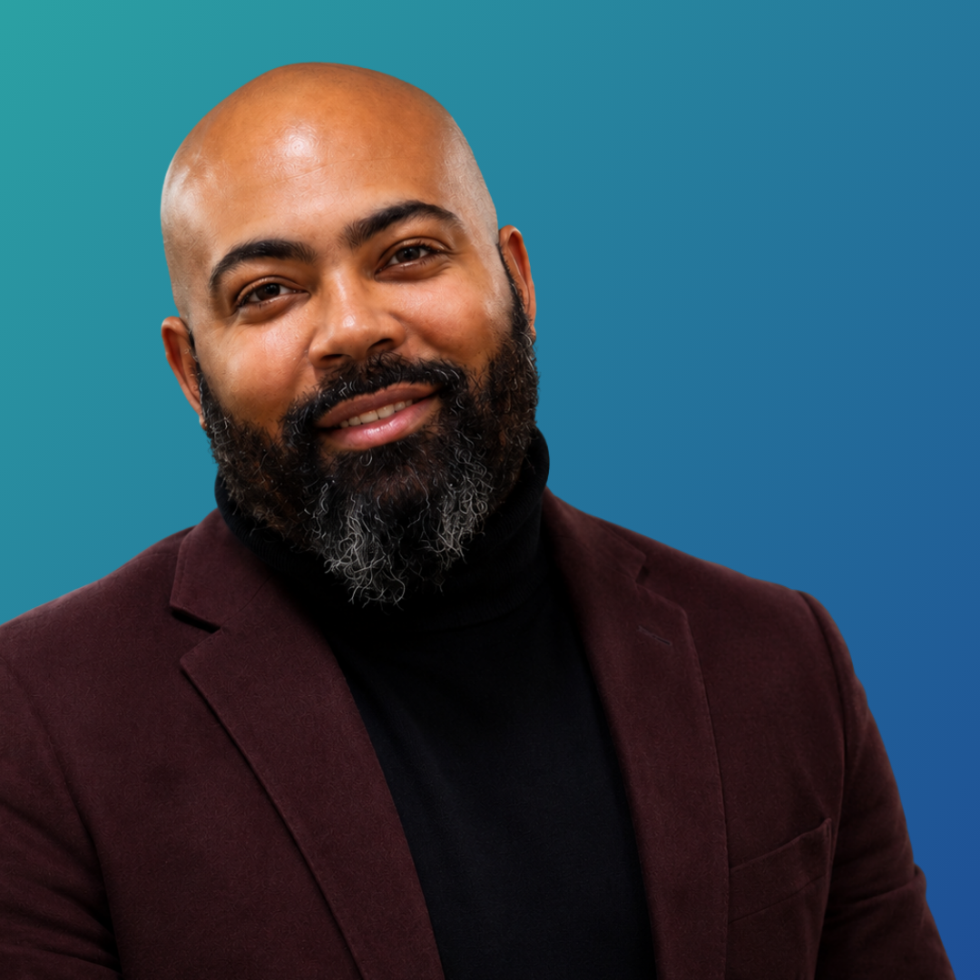 Portrait of a smiling man with a beard, wearing a black turtleneck and a burgundy blazer, against a turquoise background.