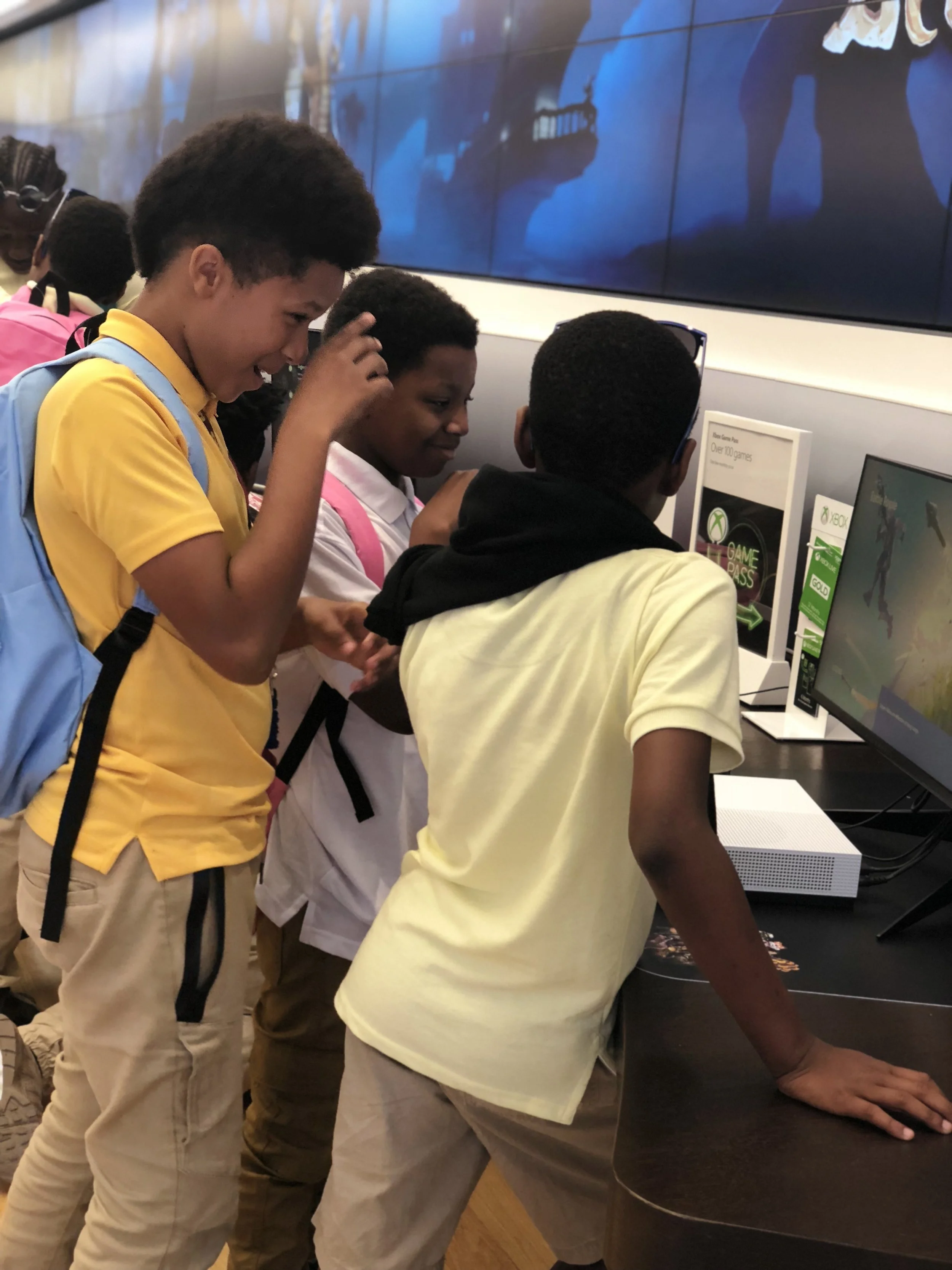 Group of children gathered around an Xbox gaming console and monitor in a store or gaming center, engaging with the video game.