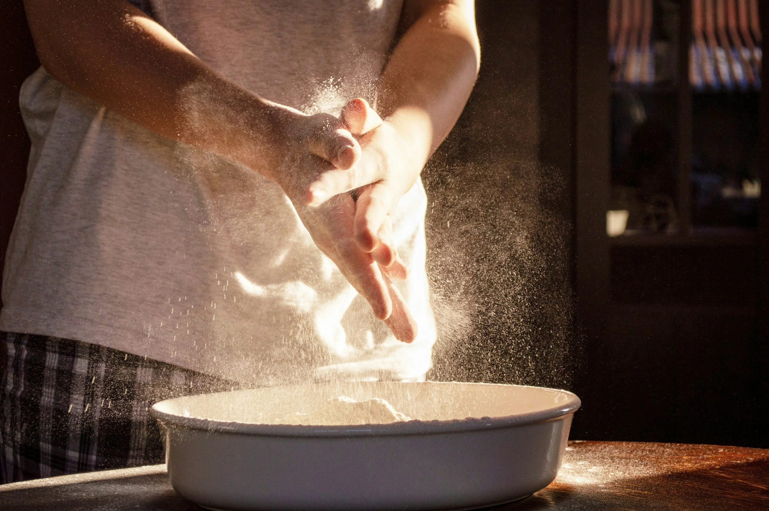 Person sifting flour into a bowl, with flour particles flying through the air.