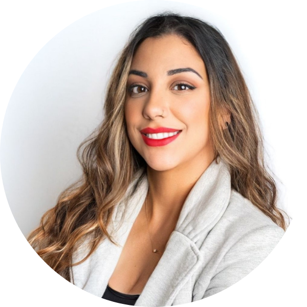 A young woman with long wavy brown hair, wearing red lipstick, smiling, dressed in a light-colored jacket, against a plain white background.