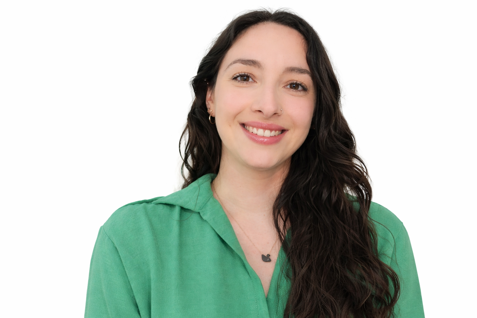 A young woman with long, dark, wavy hair, smiling, wearing a green shirt and a necklace with a black cat charm, against a white background.