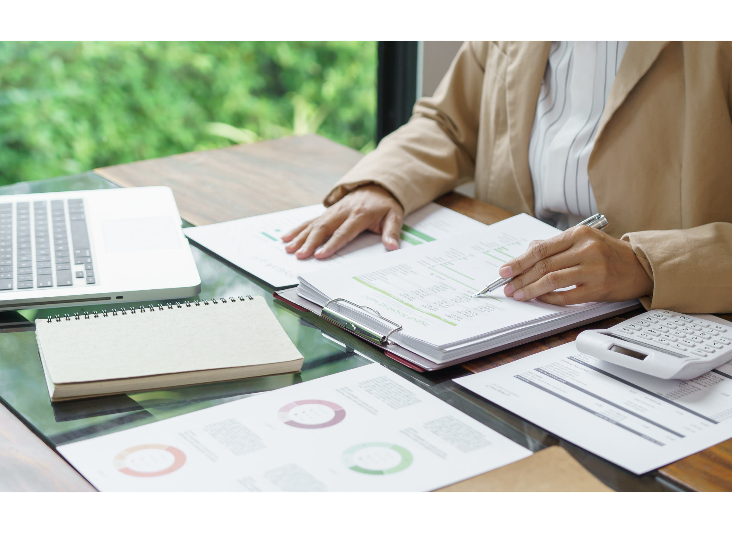 Person reviewing financial documents at a desk.
Laptop, calculator, notepad, and financial reports are on the desk.