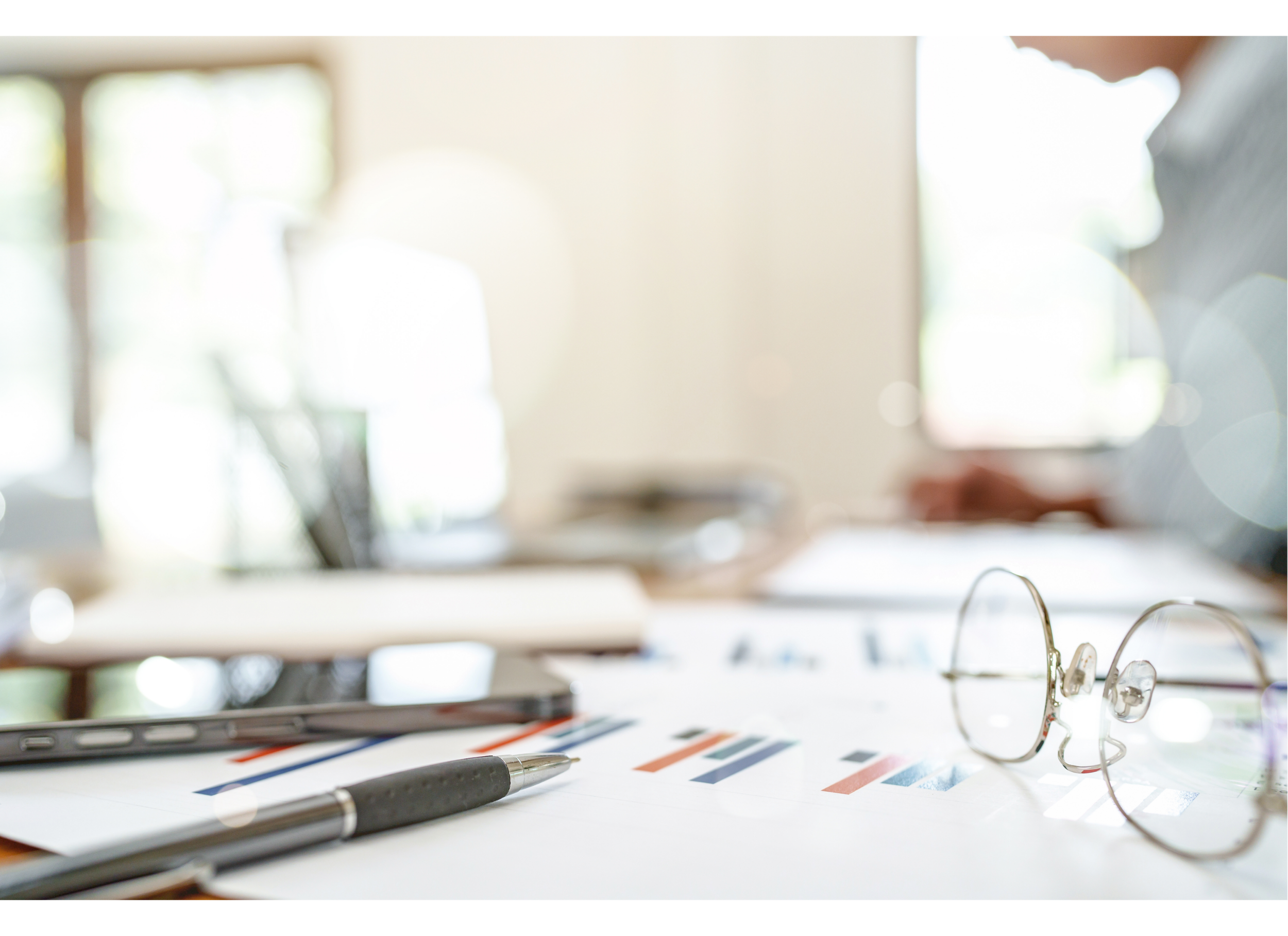 Blurred office desk with glasses, pen, and various papers and charts.