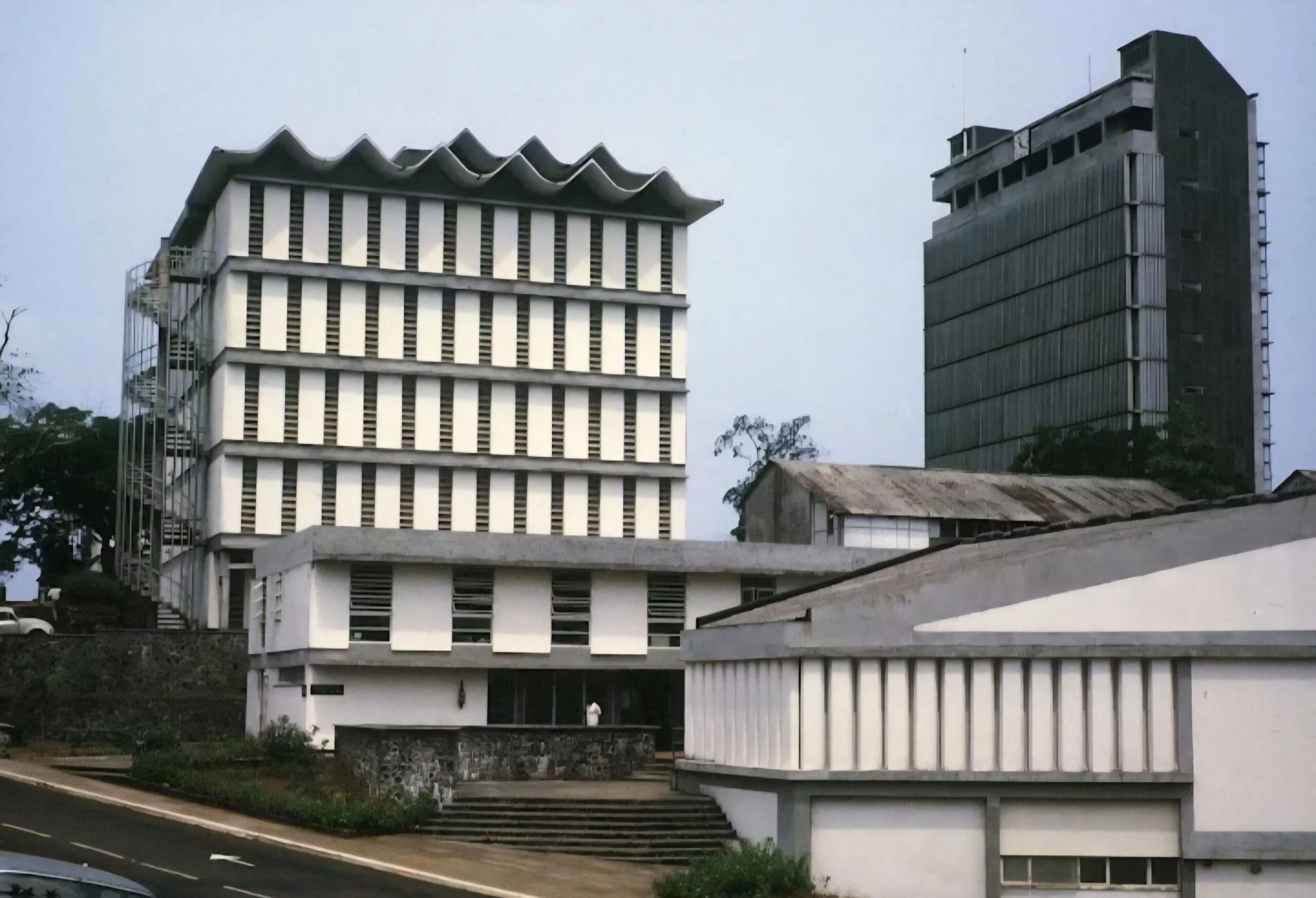 Photo of modern architecture buildings, one with a wavy roof, and the other a tall rectangular tower, set against a cloudy sky.