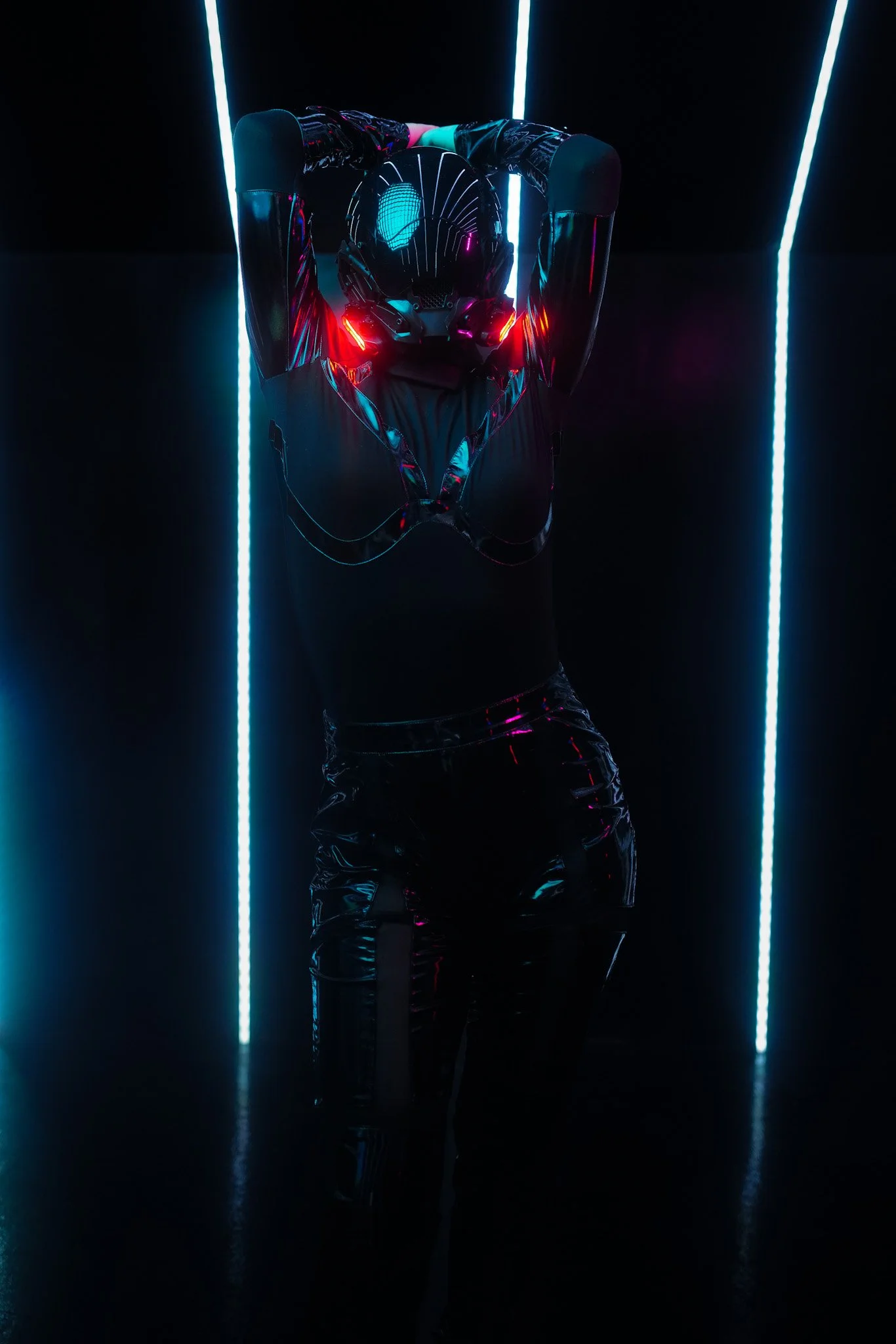 A person wearing a futuristic, shiny black outfit and a helmet with glowing red lights, standing with arms raised behind their head in a dark room with vertical blue neon lights.