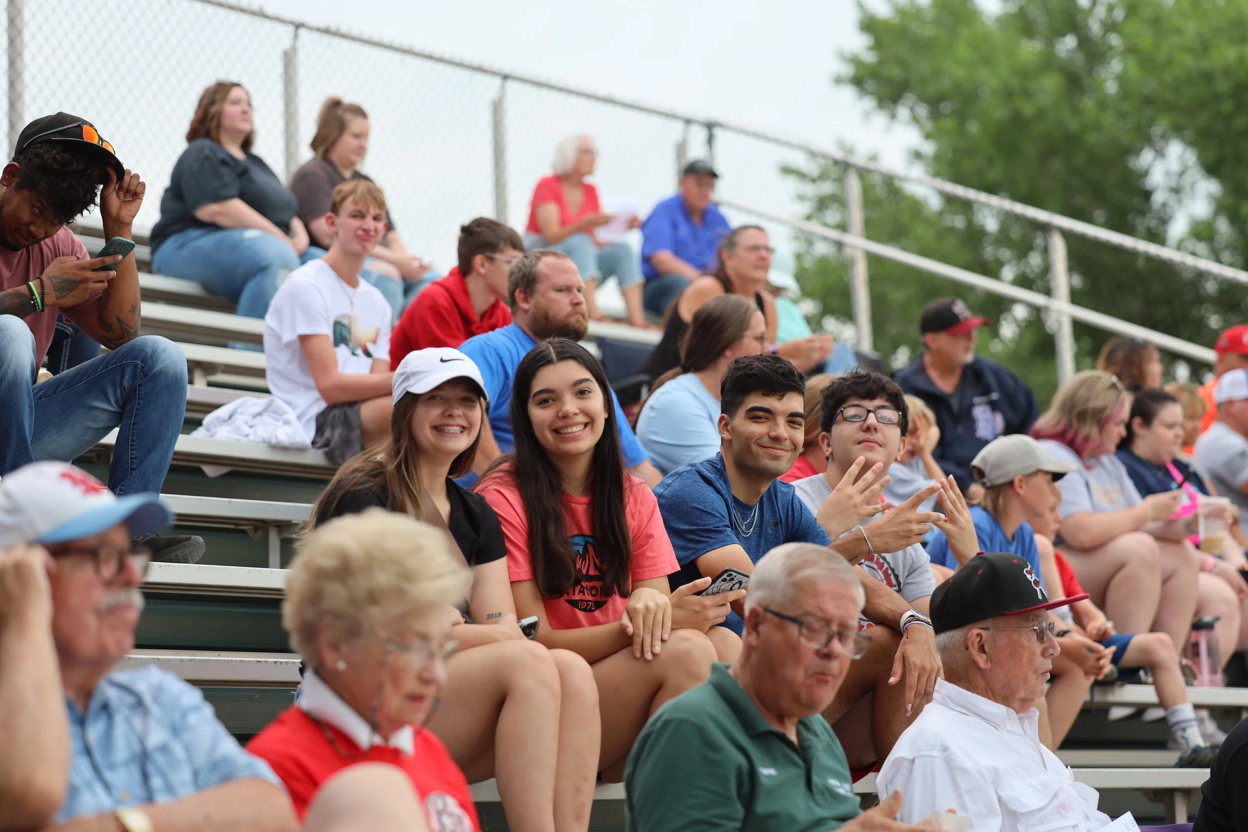 Crowd sitting on bleachers at a Bee Jays game, with some people smiling and others focused on the game.