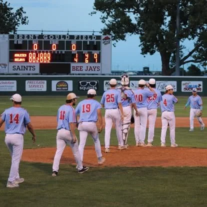 Baseball players in light blue uniforms and white caps on the field, some with numbers, walking towards the pitcher's mound with a scoreboard in the background showing a tied game and the score 4-4.