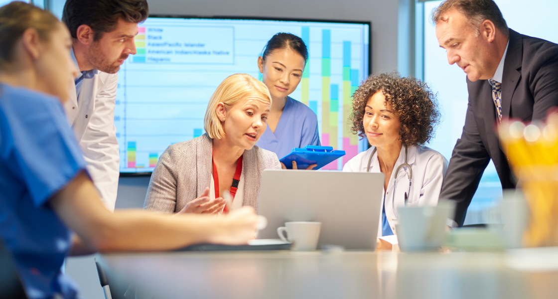 Diverse healthcare professionals and researchers collaborating around a laptop in a clinical setting.