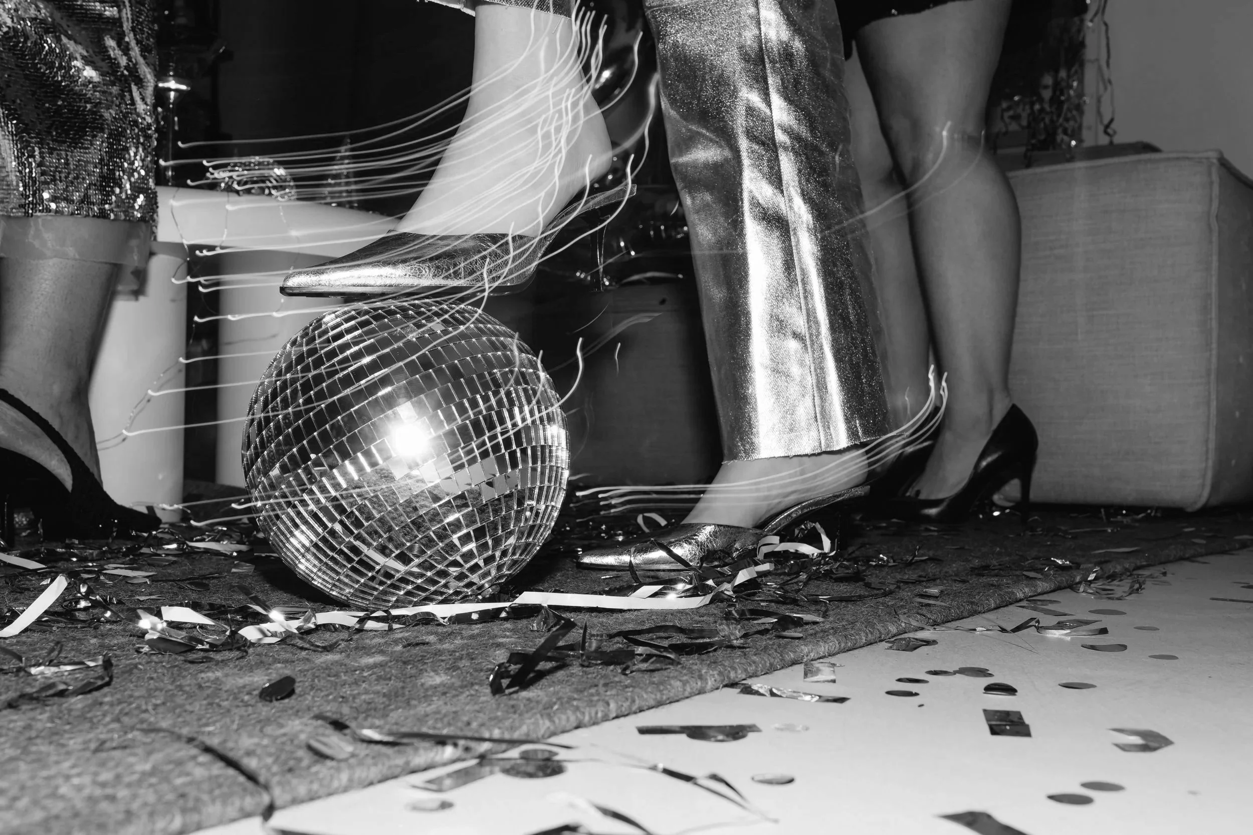 A disco ball and metallic decorations on the floor in a room with tinsel and confetti, indicating a celebration or party setting.