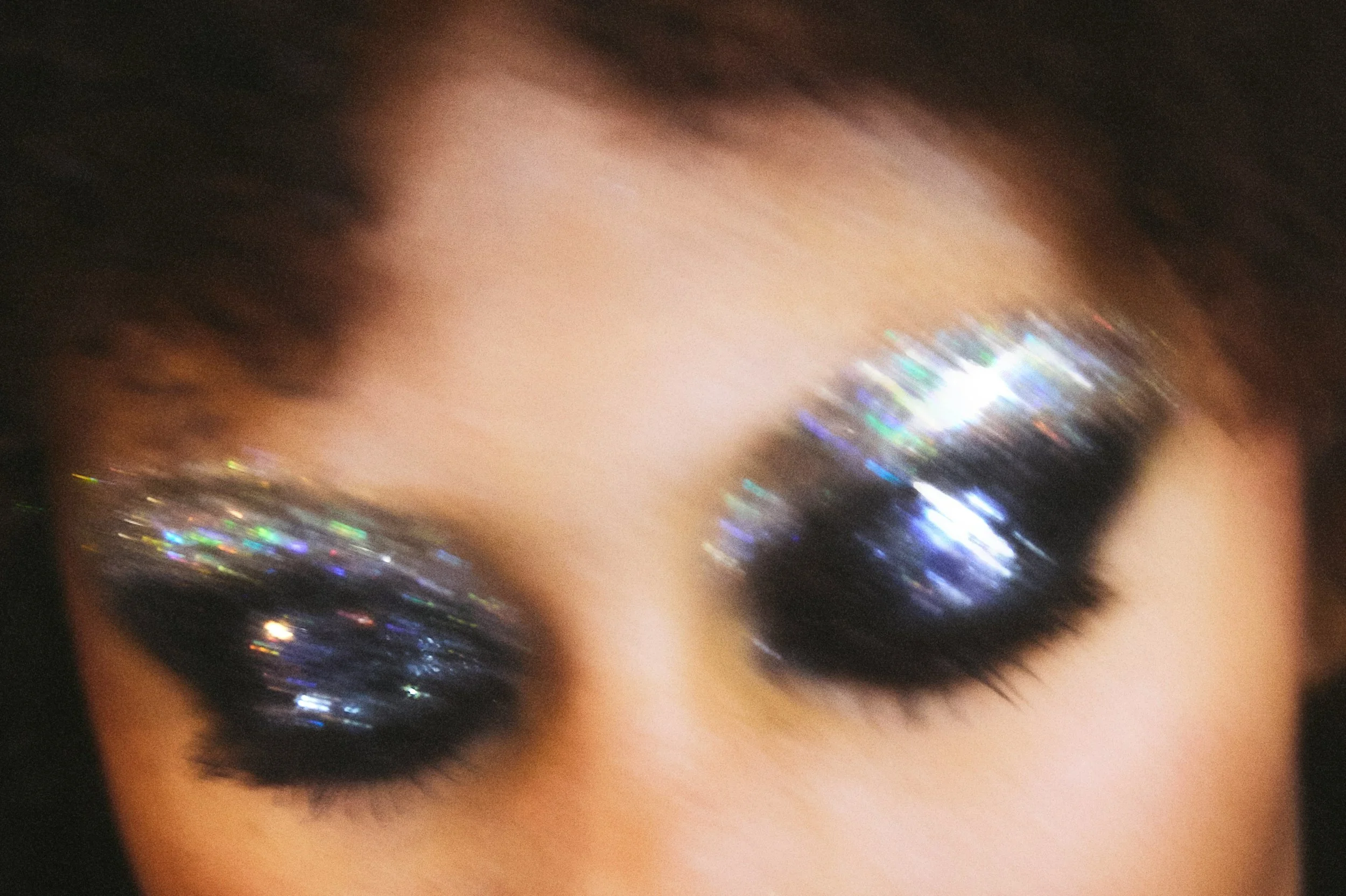 Close-up of a person's eye with dark eyeshadow and sparkly, holographic glitter on the eyelid.