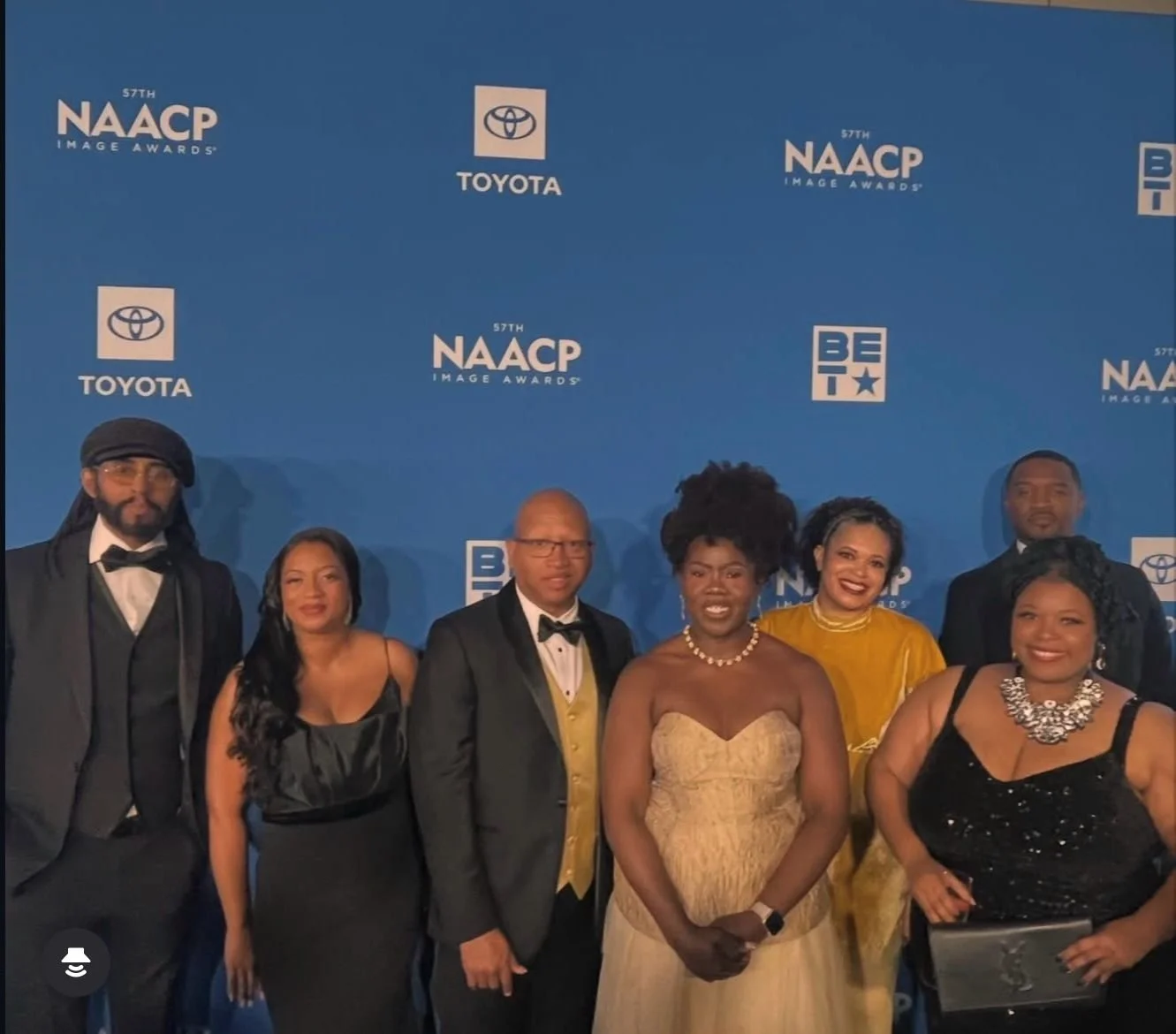 Group of seven people dressed in formal attire standing on a red carpet with a blue backdrop featuring logos for the NAACP Image Awards, Toyota, and BET.