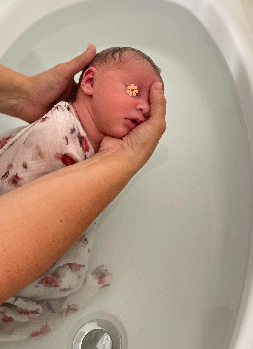 Bébé emmailloté, détendu dans l'eau. Il ferme les yeux et est légèrement sur le coté, la tête déposée dans les mains de l'accompagnatrice en périnatalité