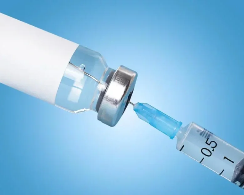 Close-up of a syringe with a needle connected to a vial, set against a blue background.