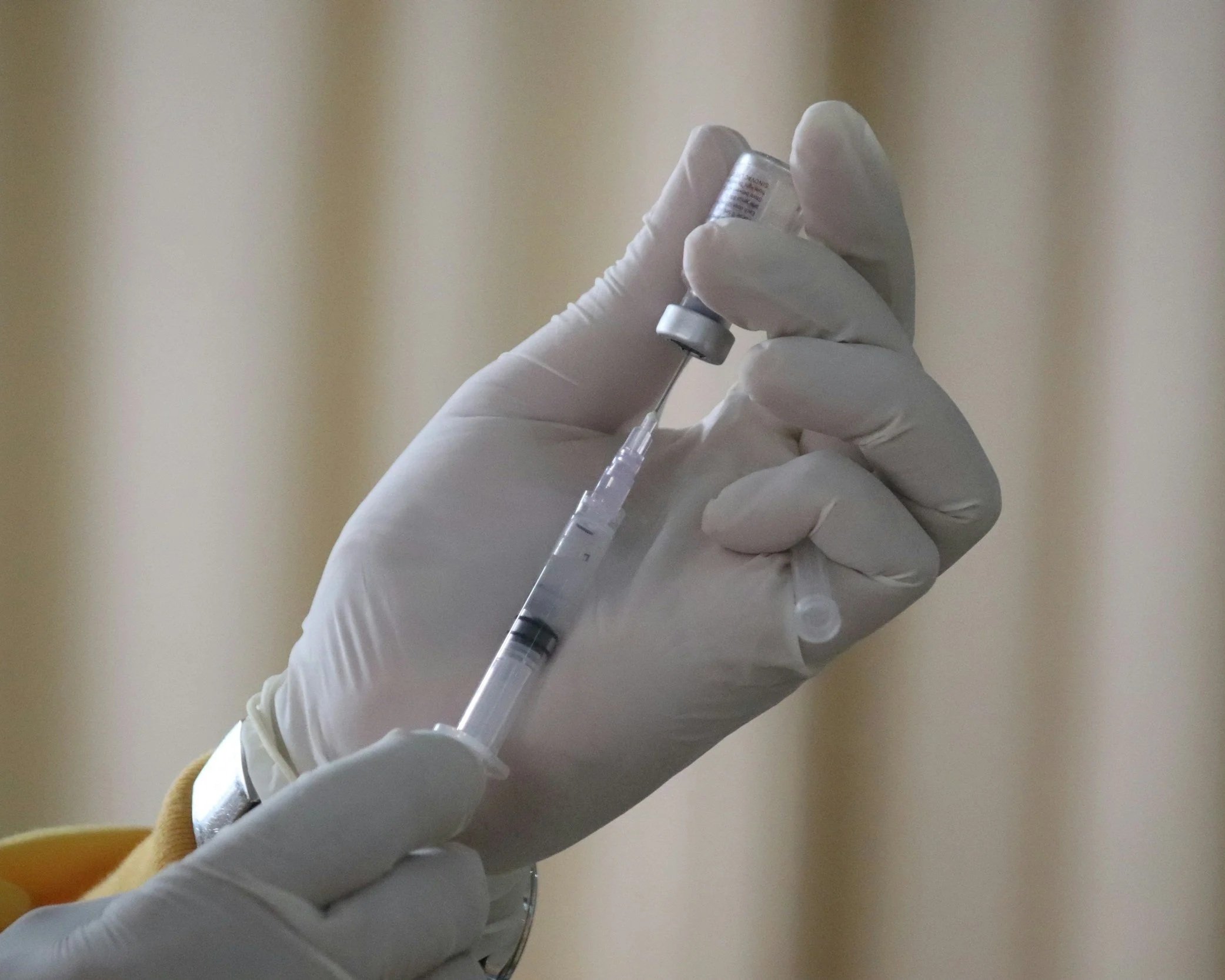 A hand wearing a white glove holding a syringe with a clear liquid inside.