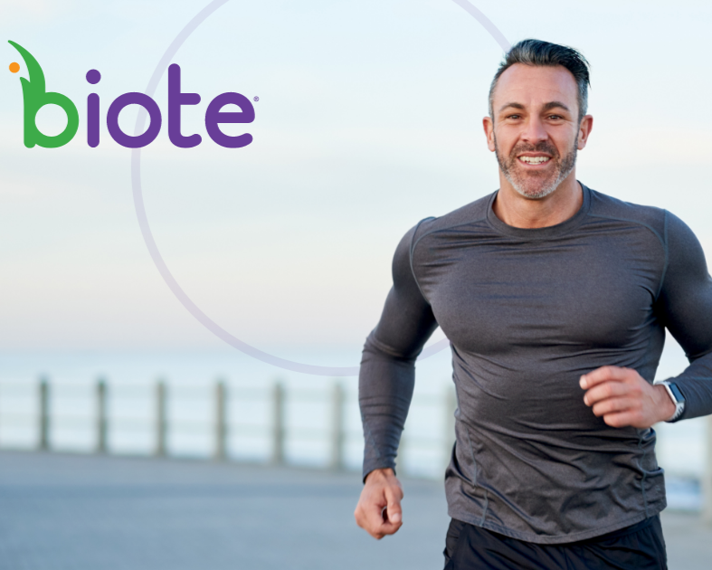 A man jogging outdoors near a body of water, smiling, wearing a dark long sleeve athletic shirt, with the Biote logo in the top left corner.