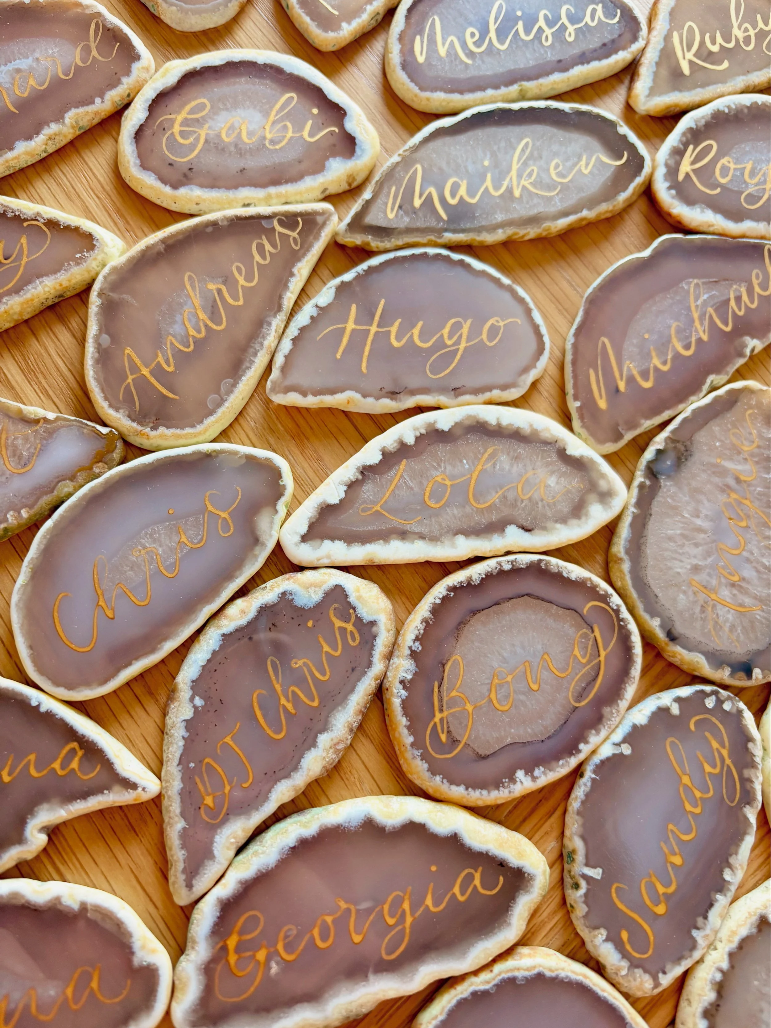 Assorted Yankee candle cookies with names written in icing, including Hugo, Loa, Georgia, and DJ Chris, arranged on a wooden surface.